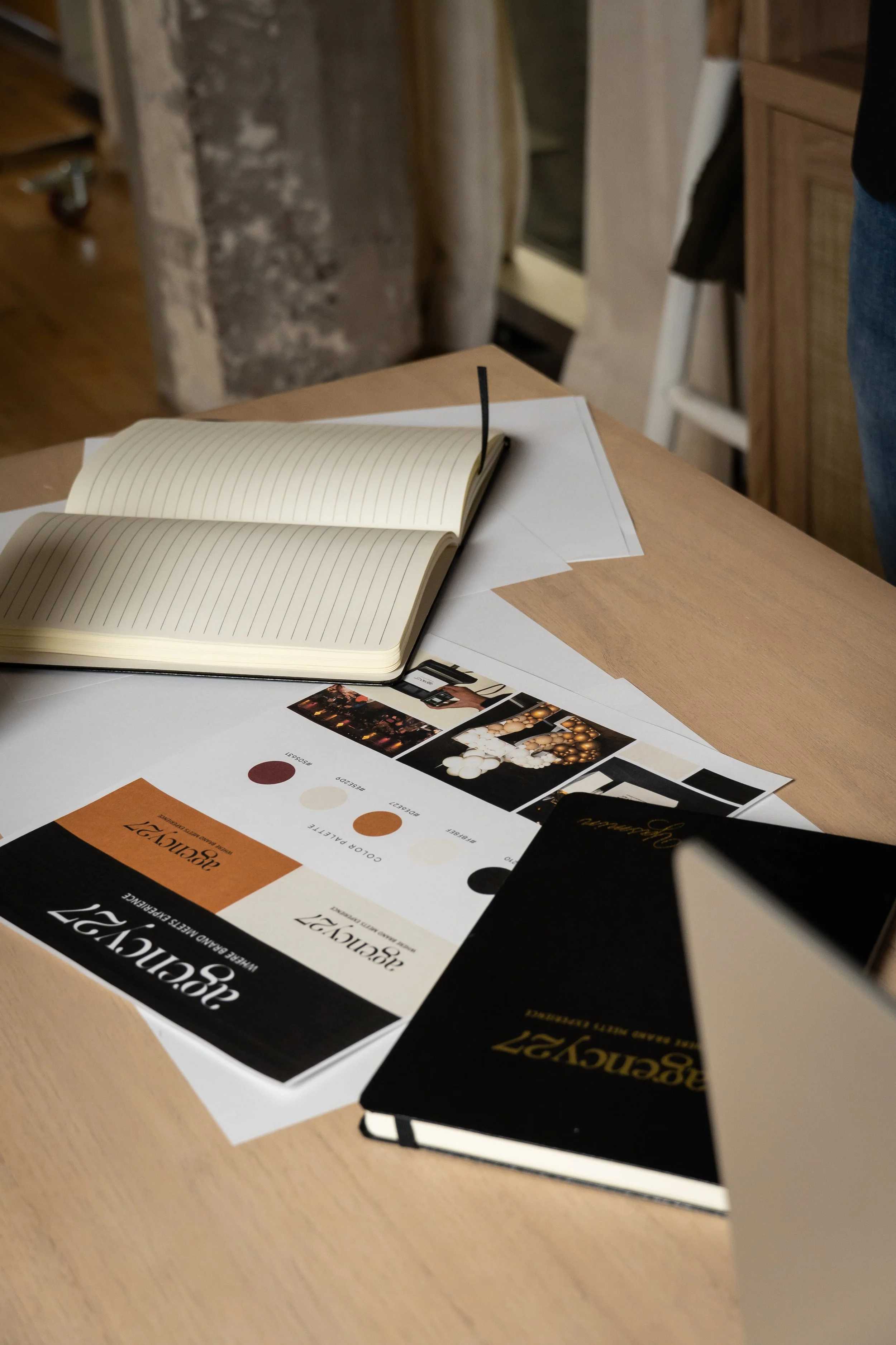 Design and branding brochure and sketchbook on a wooden table, with open prototype notebook and printed color palette and images for branding project.