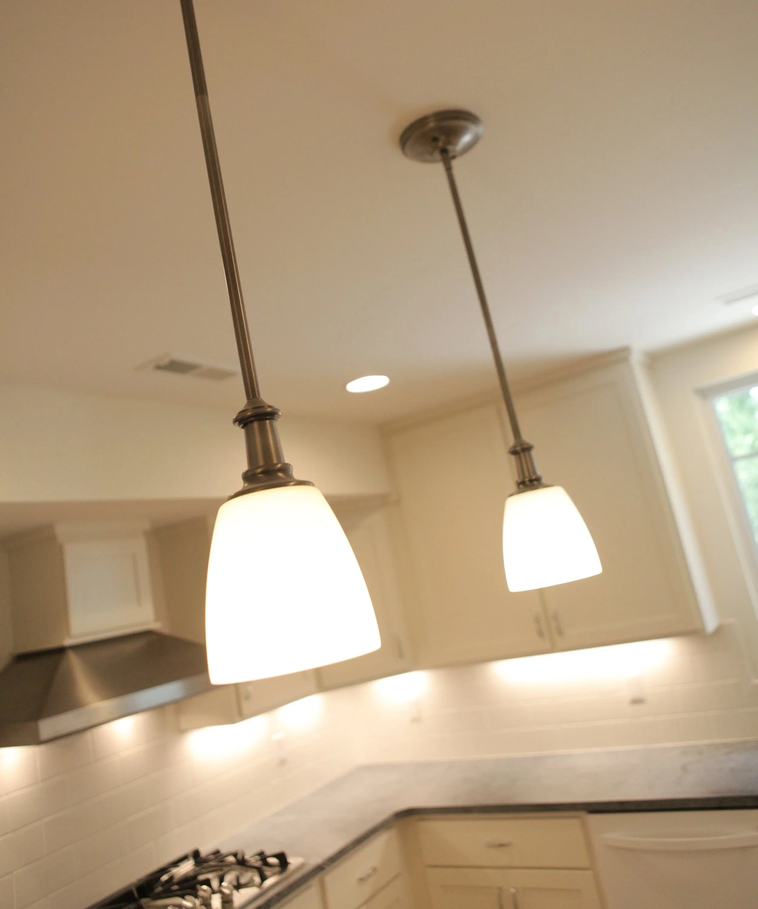 Kitchen with two pendant lights hanging from the ceiling over a granite countertop, white cabinets, and a window.