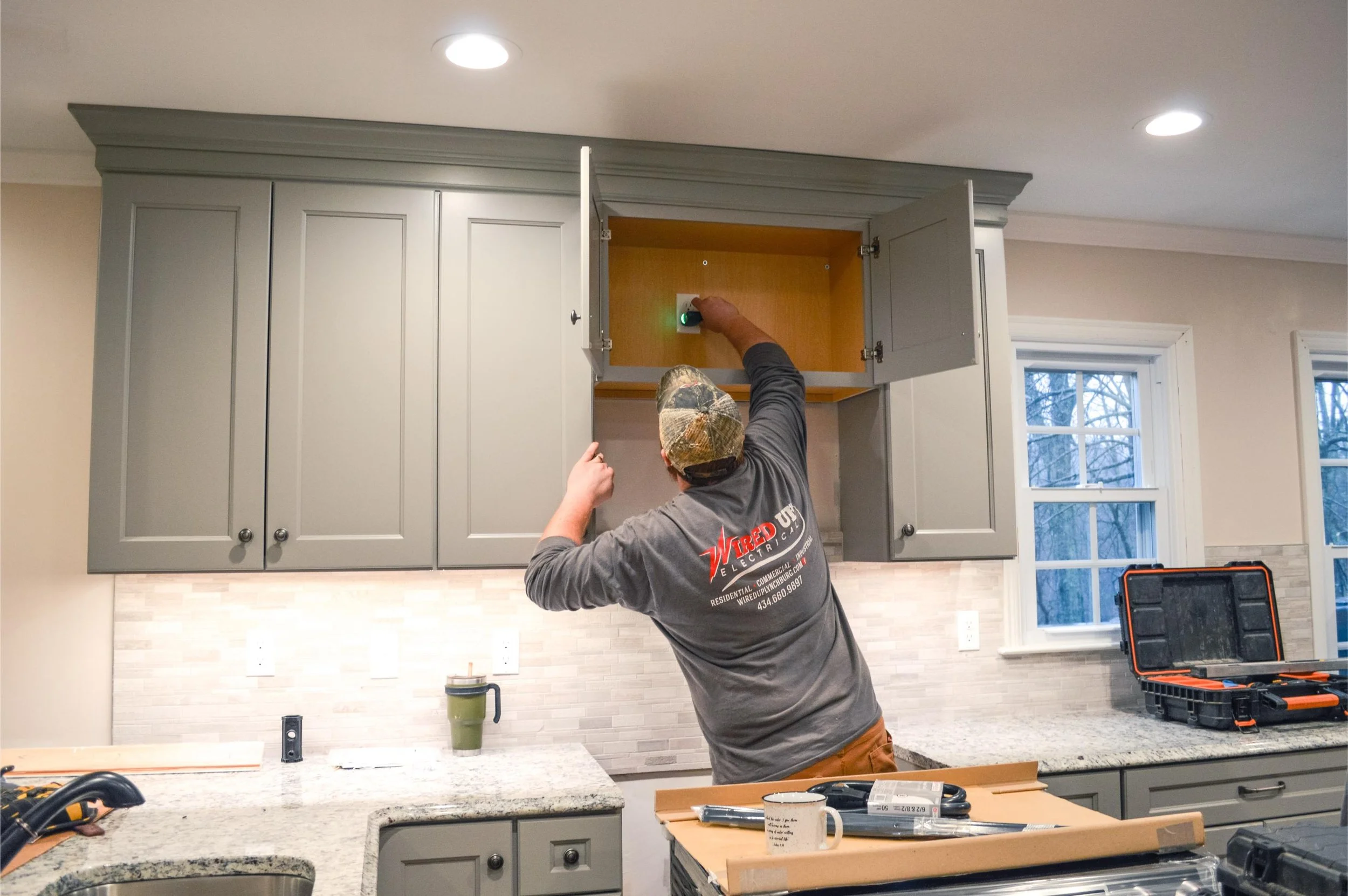 Professional electrician working inside a kitchen cabinet to install or upgrade electrical components as part of a fuse box to breaker panel conversion.