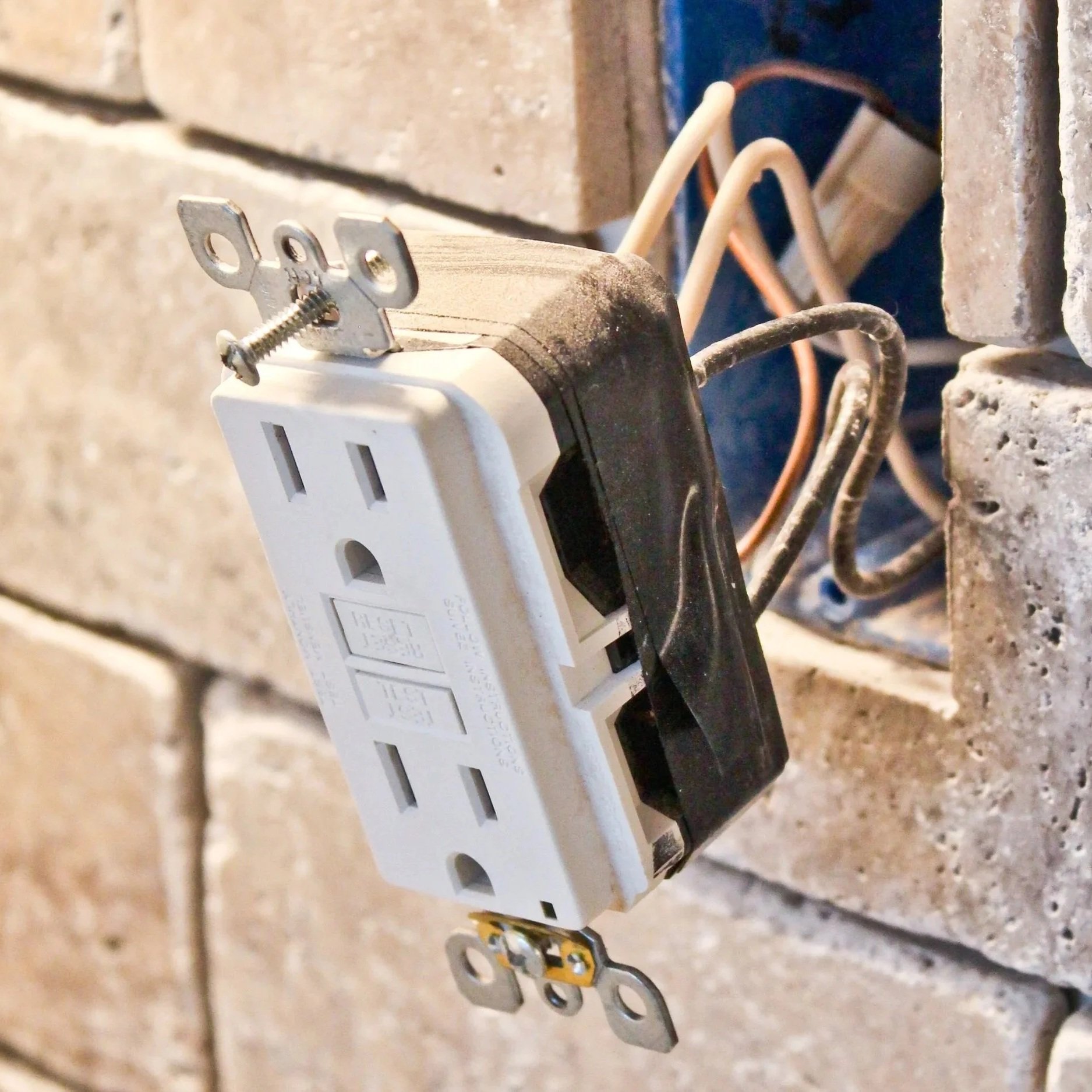 Close-up of a damaged wall outlet pulled from the electrical box, exposing wiring and demonstrating unsafe installation that needs professional repair.