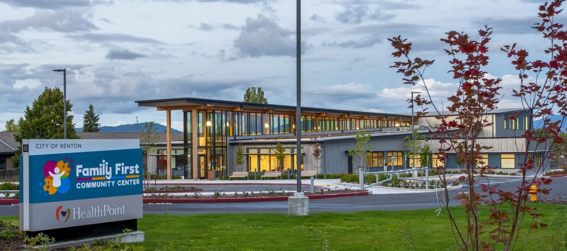 Exterior view of the Family First Community Center in Renton with a sign in the foreground, a modern building with large windows, and trees around it during daytime.