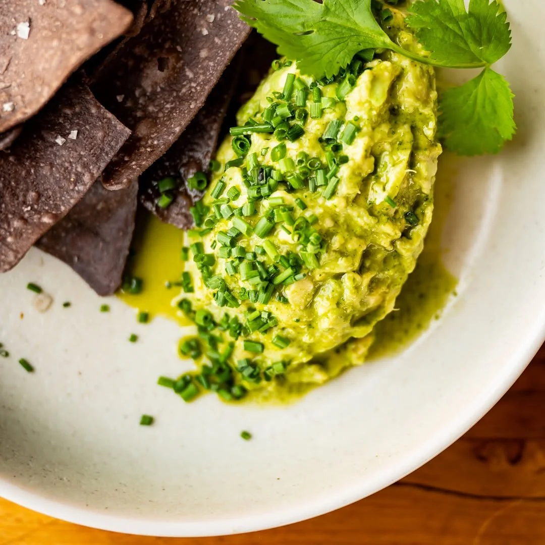 Close-up of a white bowl with slices of cooked liver, a scoop of guacamole topped with chopped chives, and garnished with cilantro leaves.