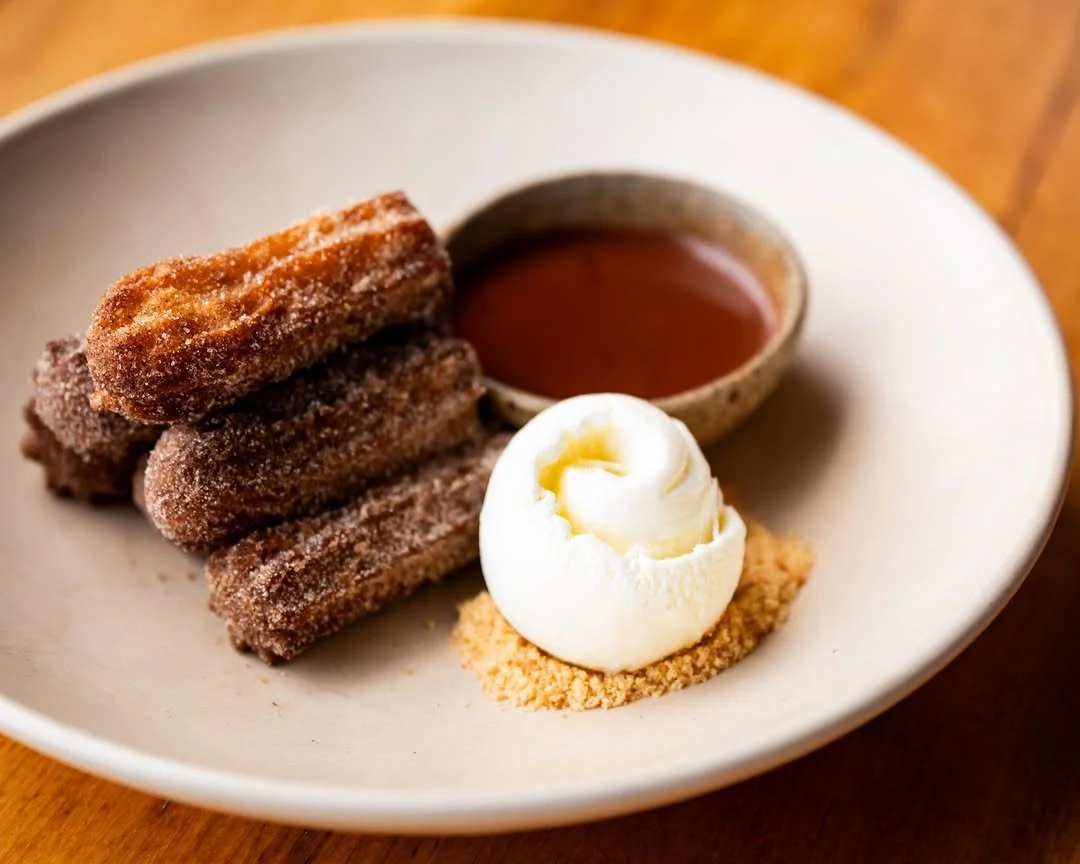 Plate of churros with chocolate sauce and a dollop of whipped cream.