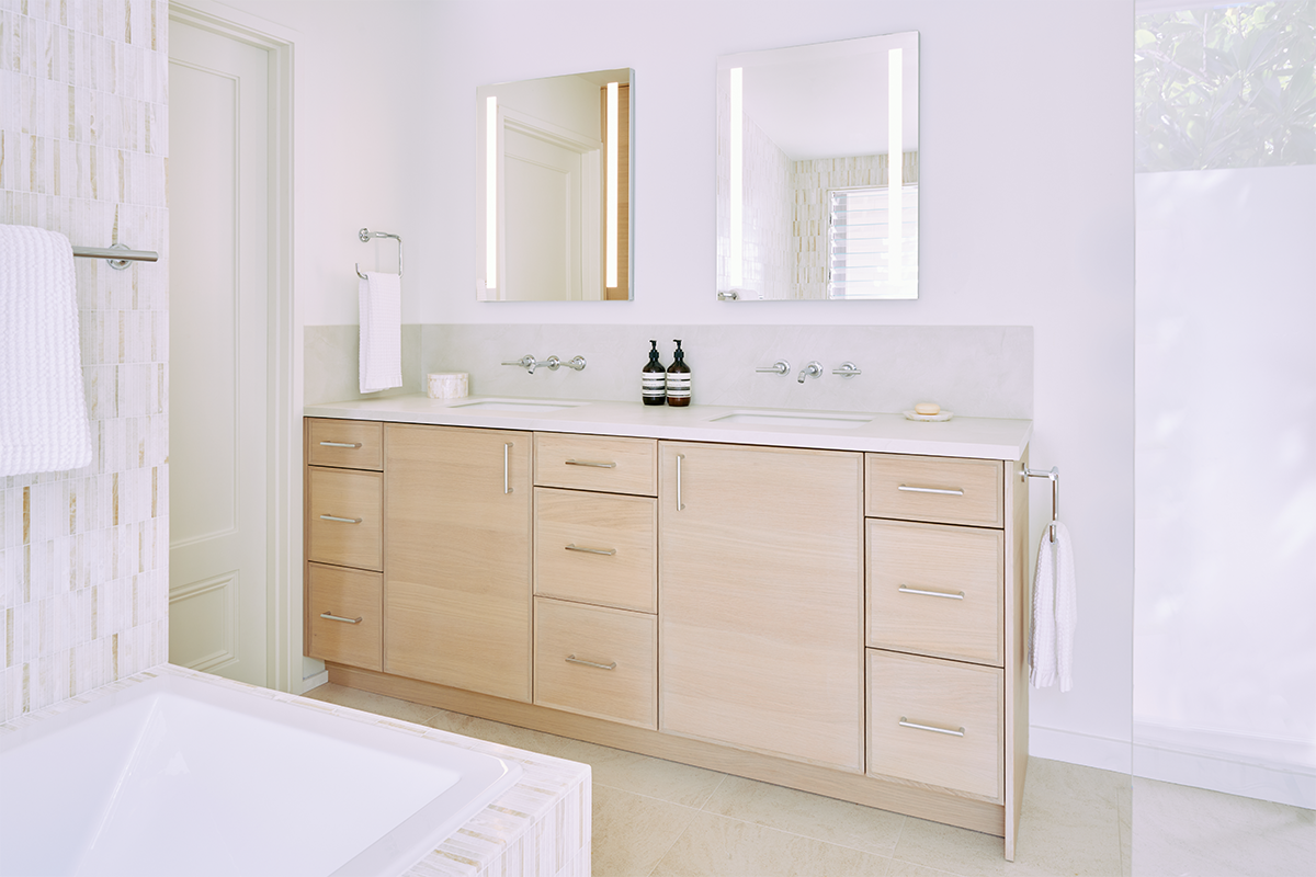 This vanity features light rift oak wood veneer cabinets and porcelain countertops. Luxury brand medicine cabinets create a perimeter glow.