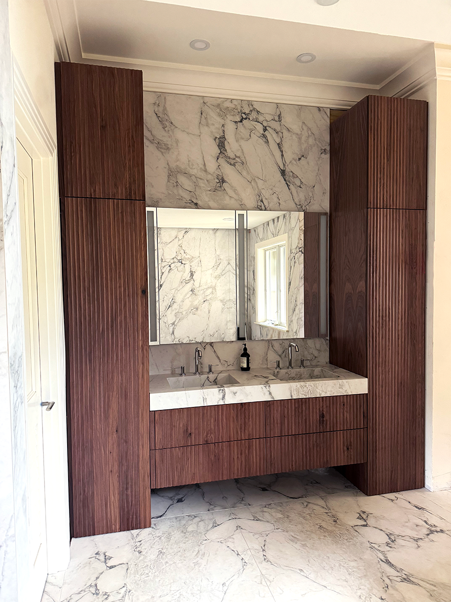 This renovated bathroom received a much needed face lift with new porcelain slabs throughout blending into the integrated sink. New custom built fluted cabinets encase the vanity creating a sense of opulence.