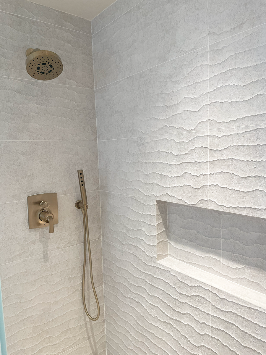 This guest bathroom shower includes textured porcelain tile which brings in character while maintaining the sense of calm the overall house evokes. The brass fixtures bring elegance to the design.