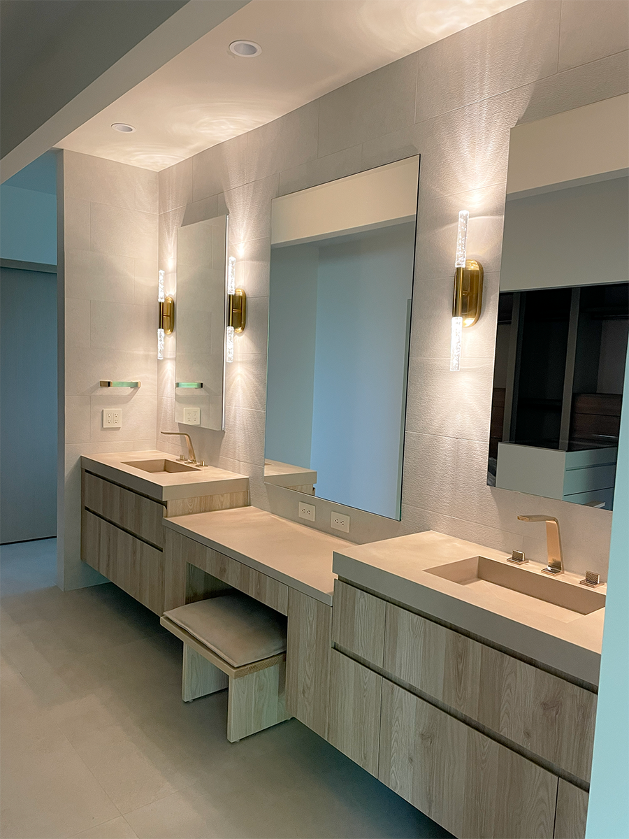 This primary bathroom creates a feeling of zen through textured limestone tile and light toned Italian millwork. The decorative light fixtures bring in some glam to the space with reeded glass and brass accents.