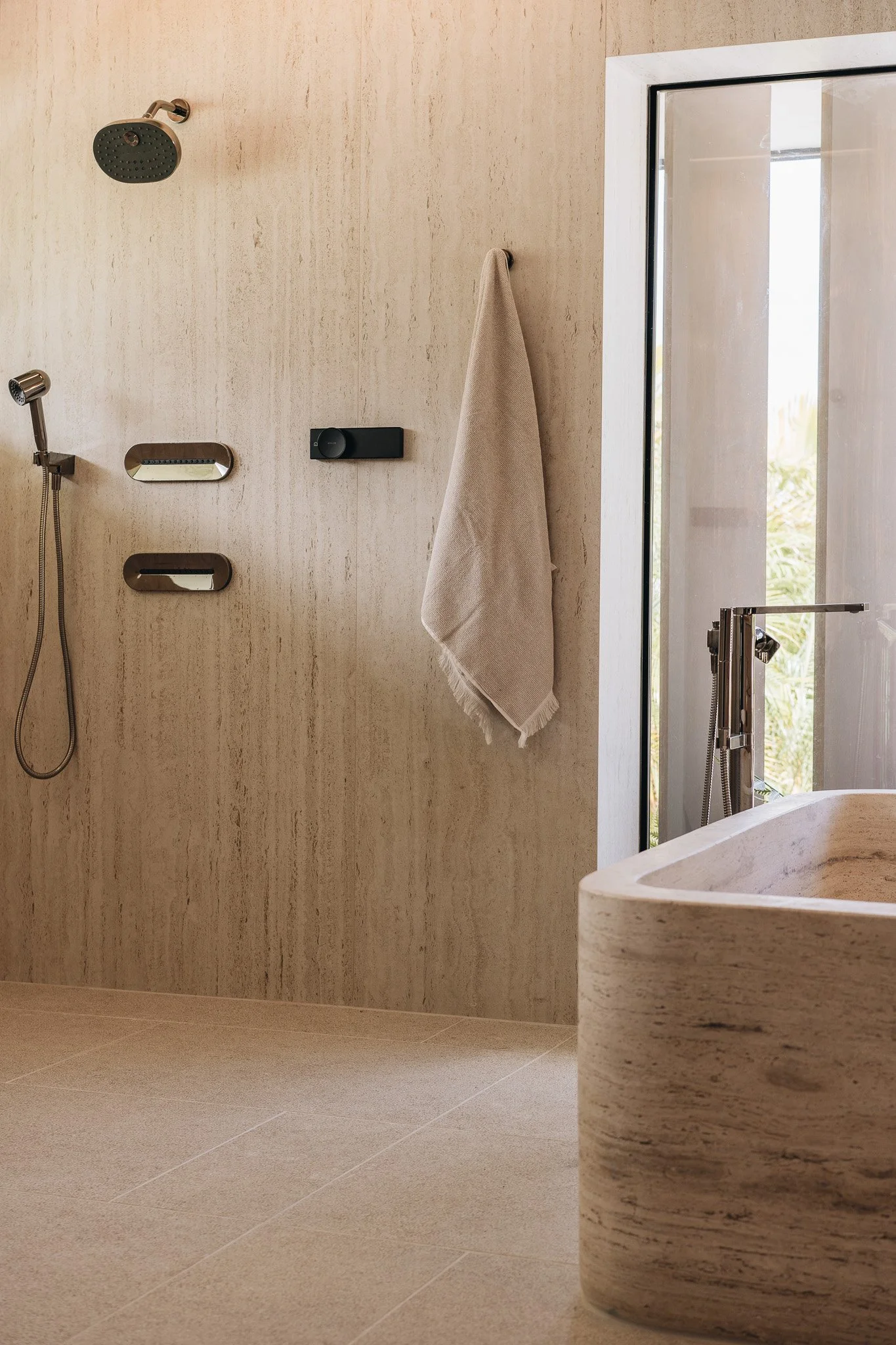Primary Bathroom with Dekton shower walls, travertine bathtub, & Kohler bronze plumbing fixtures.