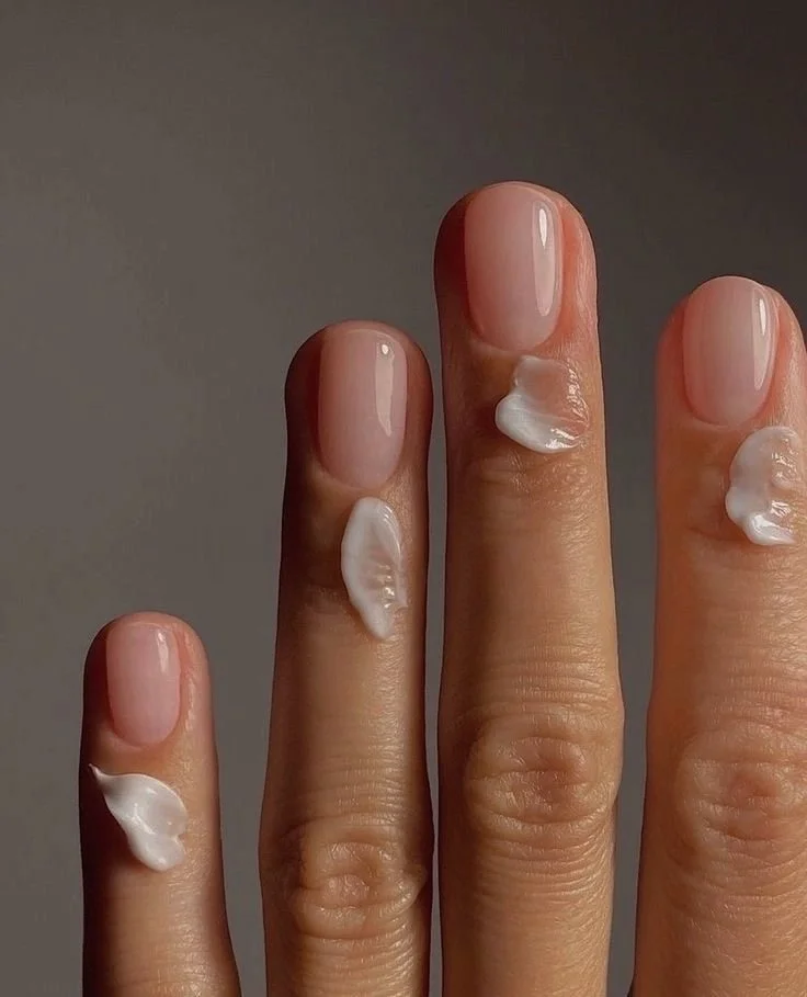 Close-up of four fingers with dollops of white cream on each fingertip and finger joint, against a neutral background.