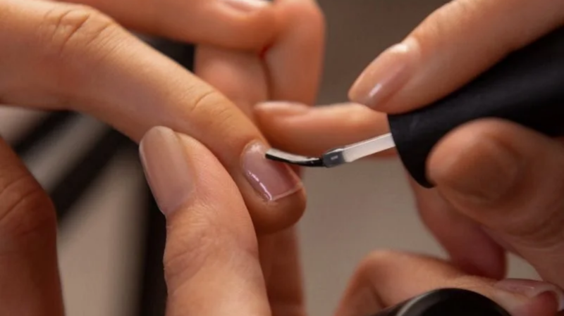 Close-up of a person receiving a manicure, with someone applying nail polish or a similar treatment to their fingernail.