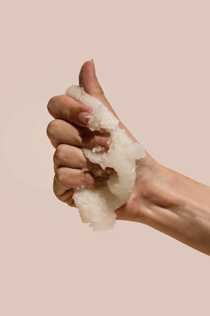 Hand holding a thumbs-up gesture covered with white salt crystals against a plain light background.