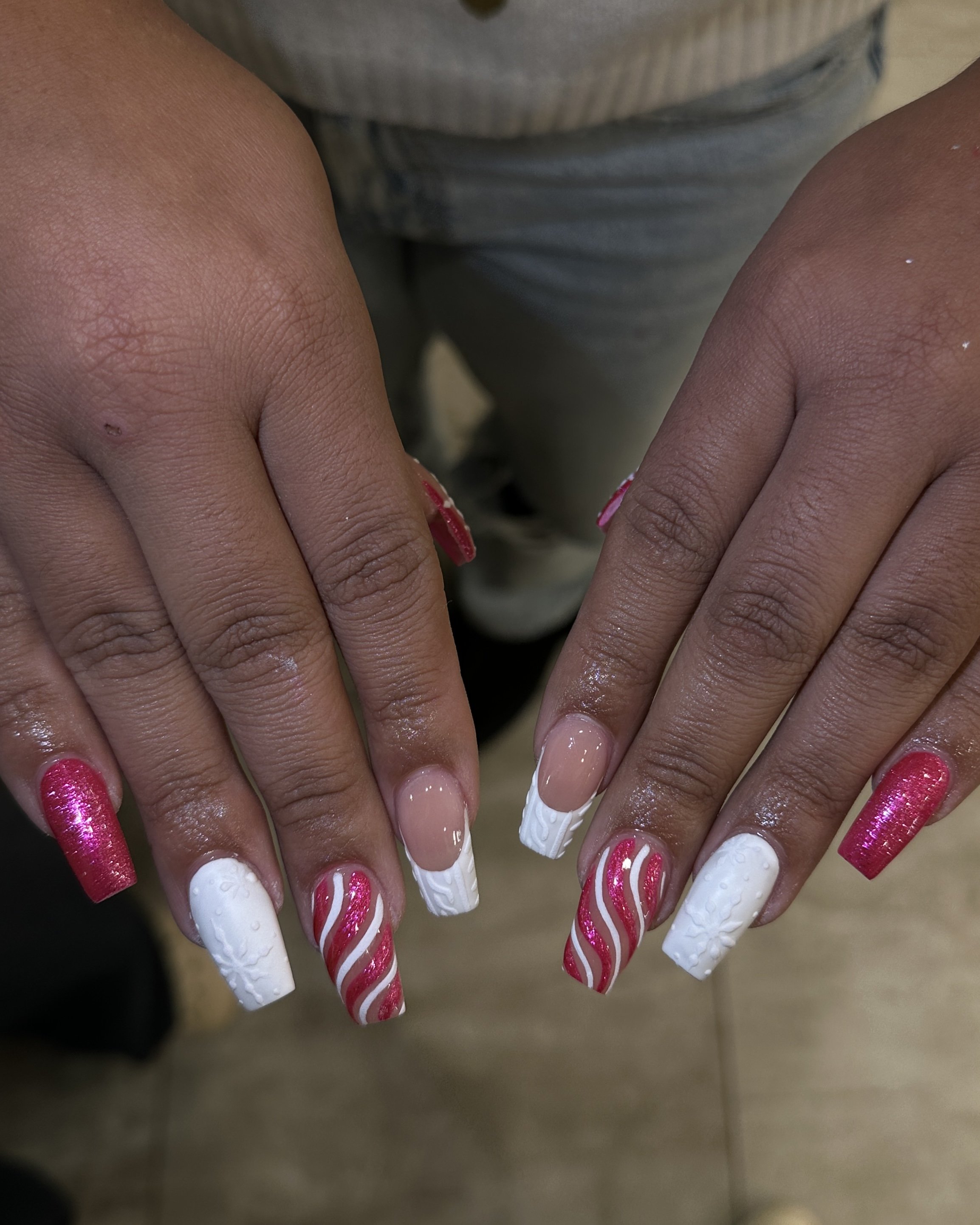 Close-up of hands with decorated nails in white, pink, and red, with a textured floral design and glitter.