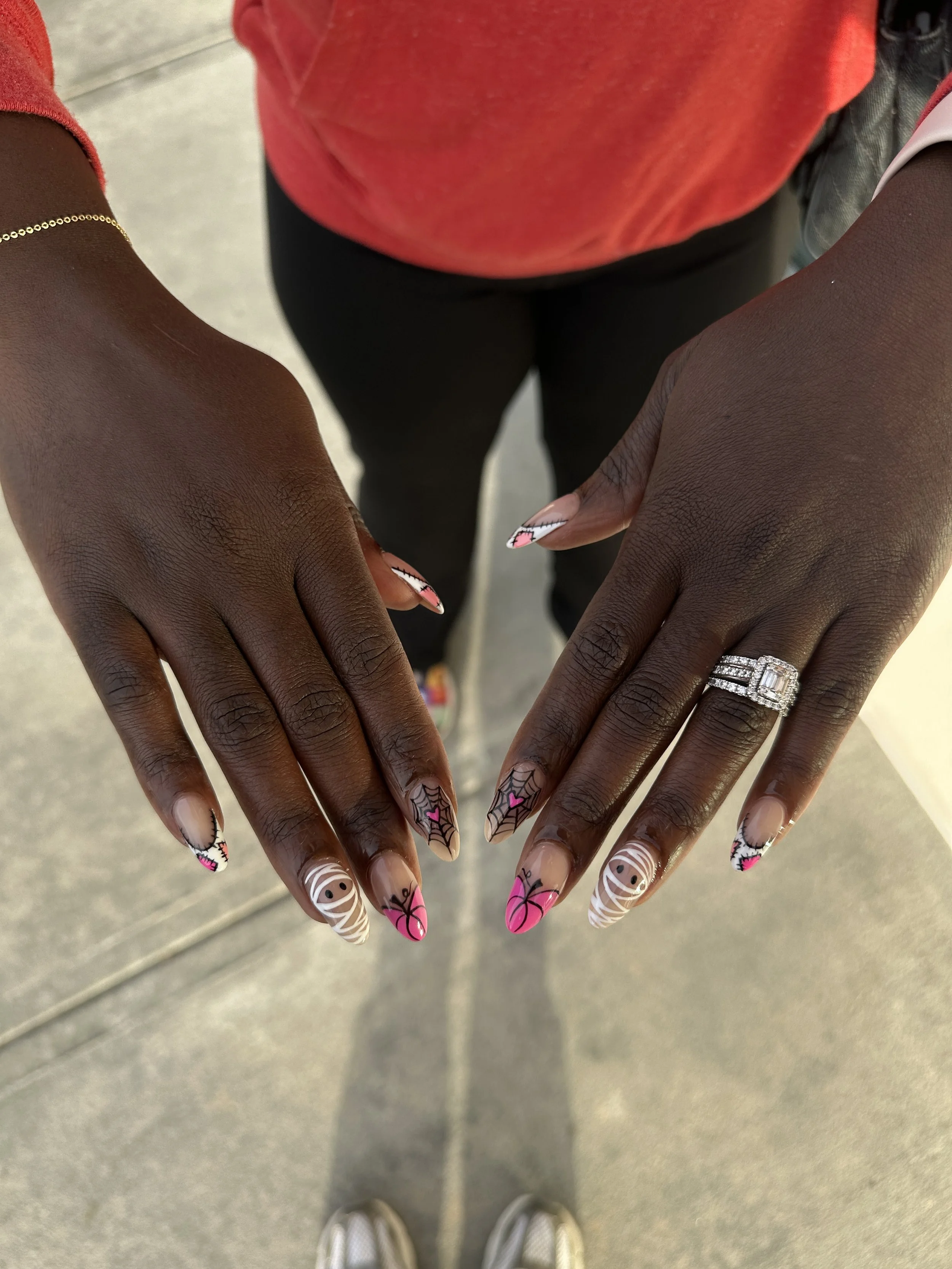 Close-up of hands showing colorful Halloween-themed nail art, including spiders and spiders web designs, with a wedding ring on the right hand.