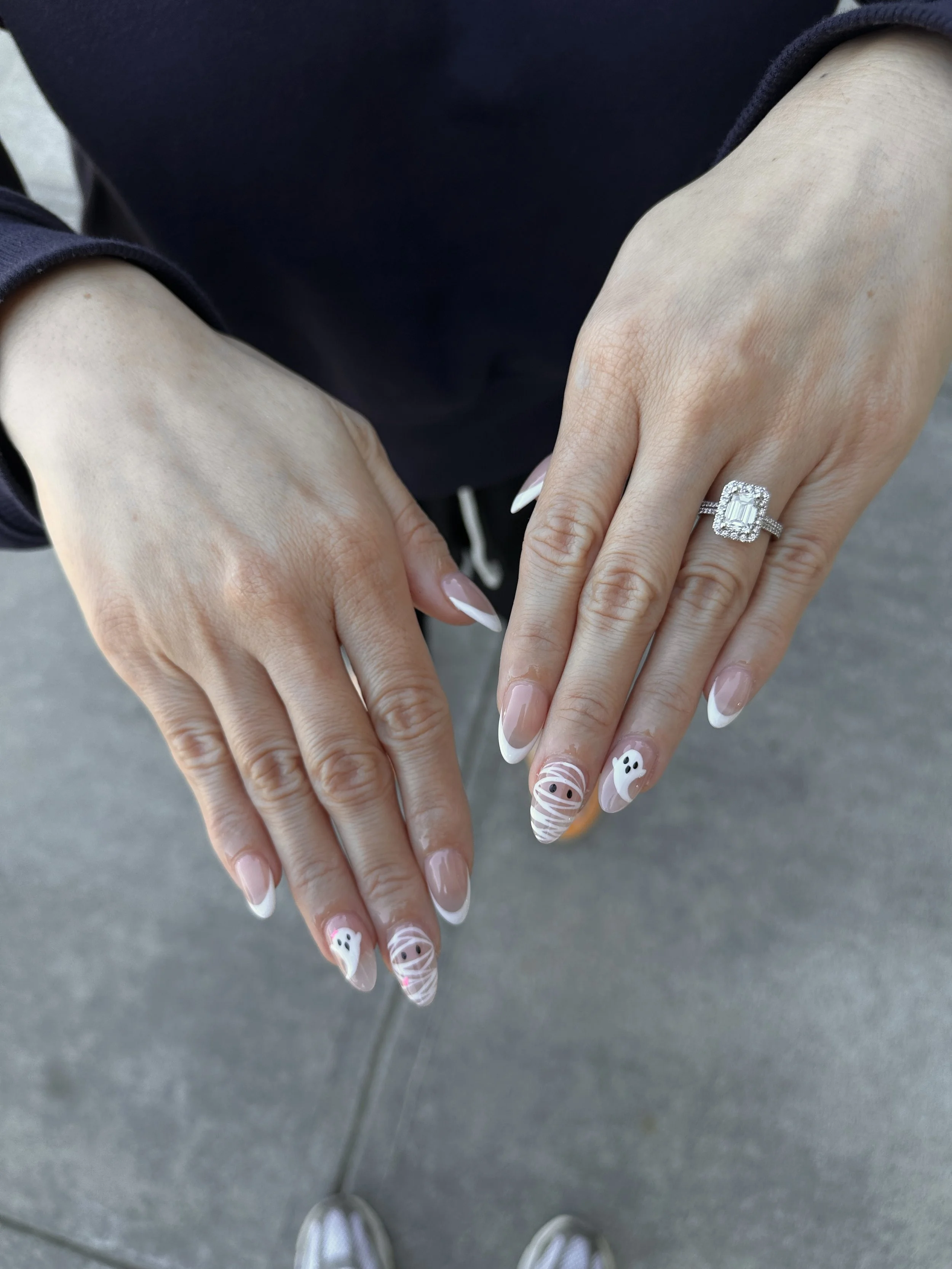 Woman's hands displaying Halloween-themed nail art and a silver ring with a large rectangular diamond surrounded by smaller diamonds.