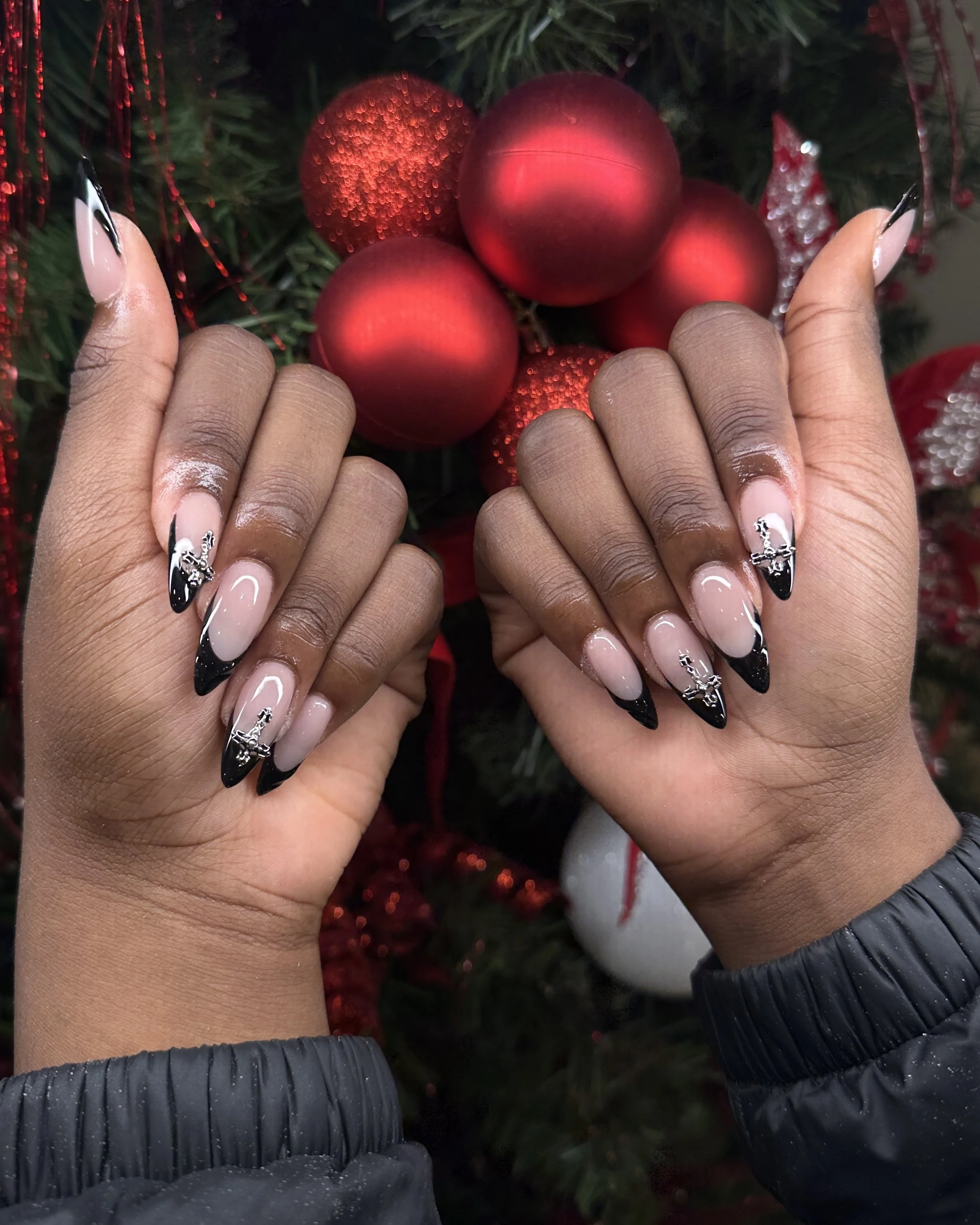 Close-up of hands with decorated black and white French manicure nails, holding red Christmas ornaments on a Christmas tree.