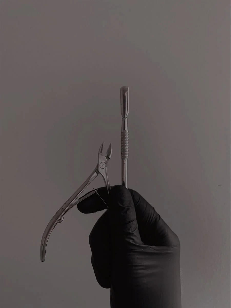 A hand wearing a black glove holding dental surgical instruments against a plain gray background.