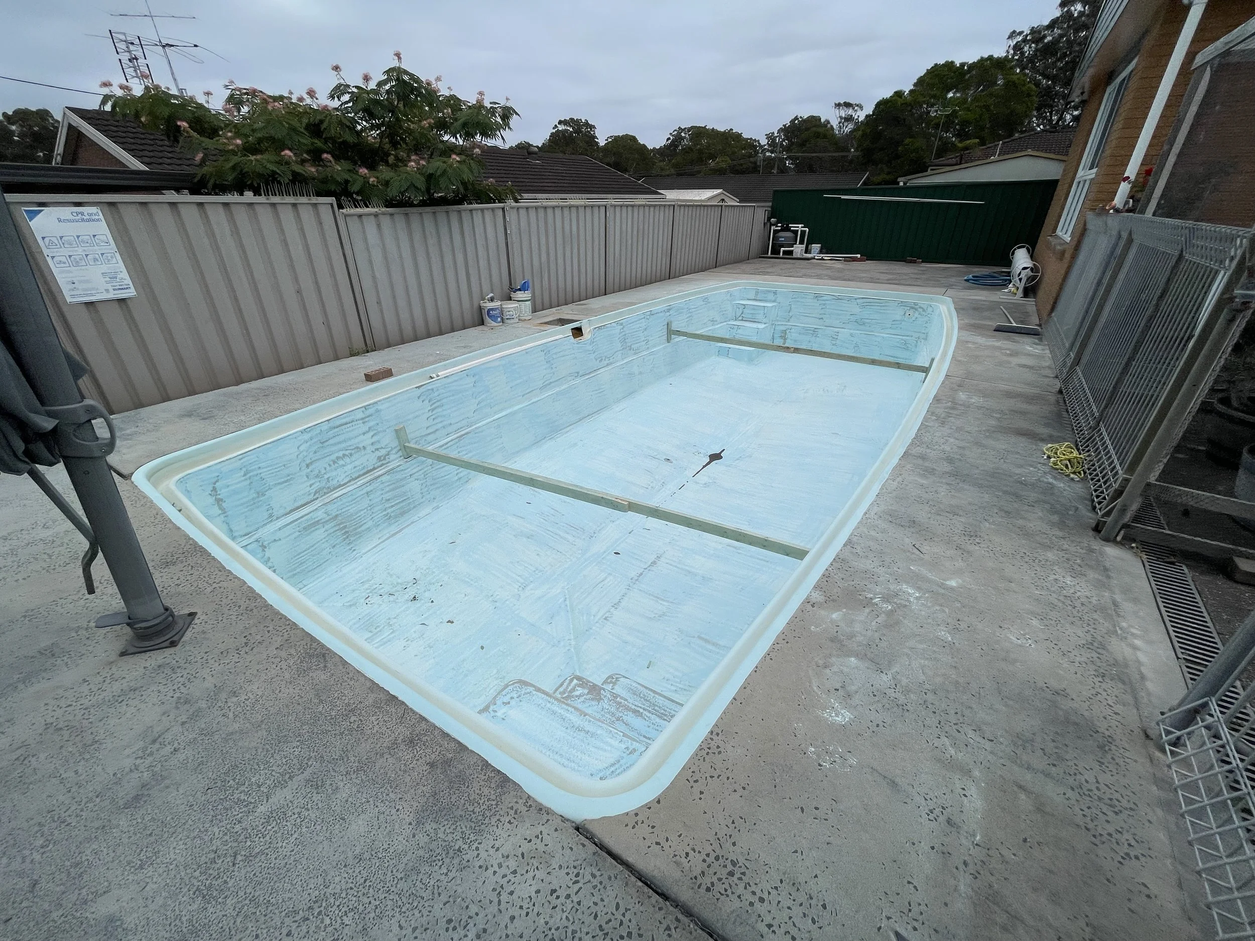 Empty swimming pool under construction on a concrete deck in a backyard.