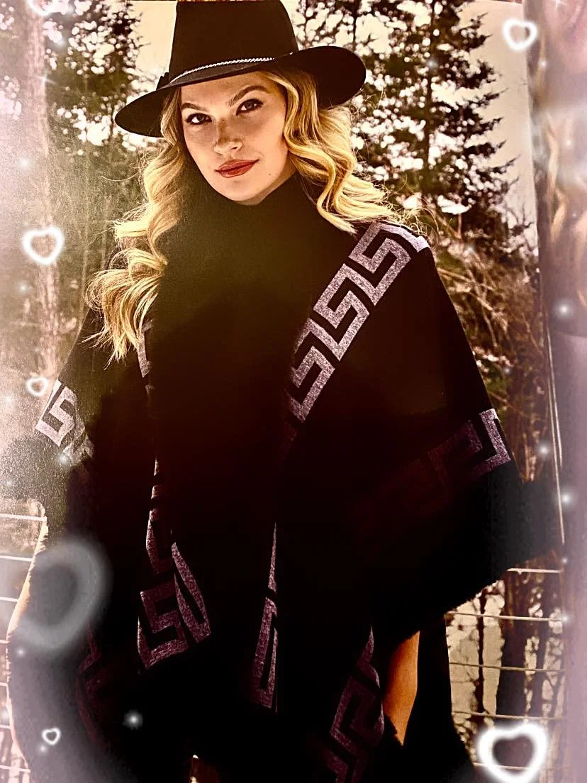 A young woman with blonde wavy hair wearing a black wide-brimmed hat and a black turtleneck, standing outdoors in front of trees during sunset, with heart-shaped and glowing light effects around her.