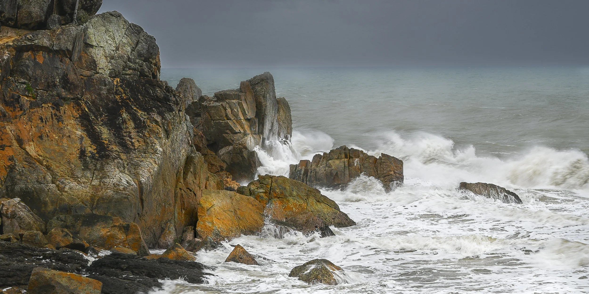 Windy shoreline with large rocks and crashing waves.