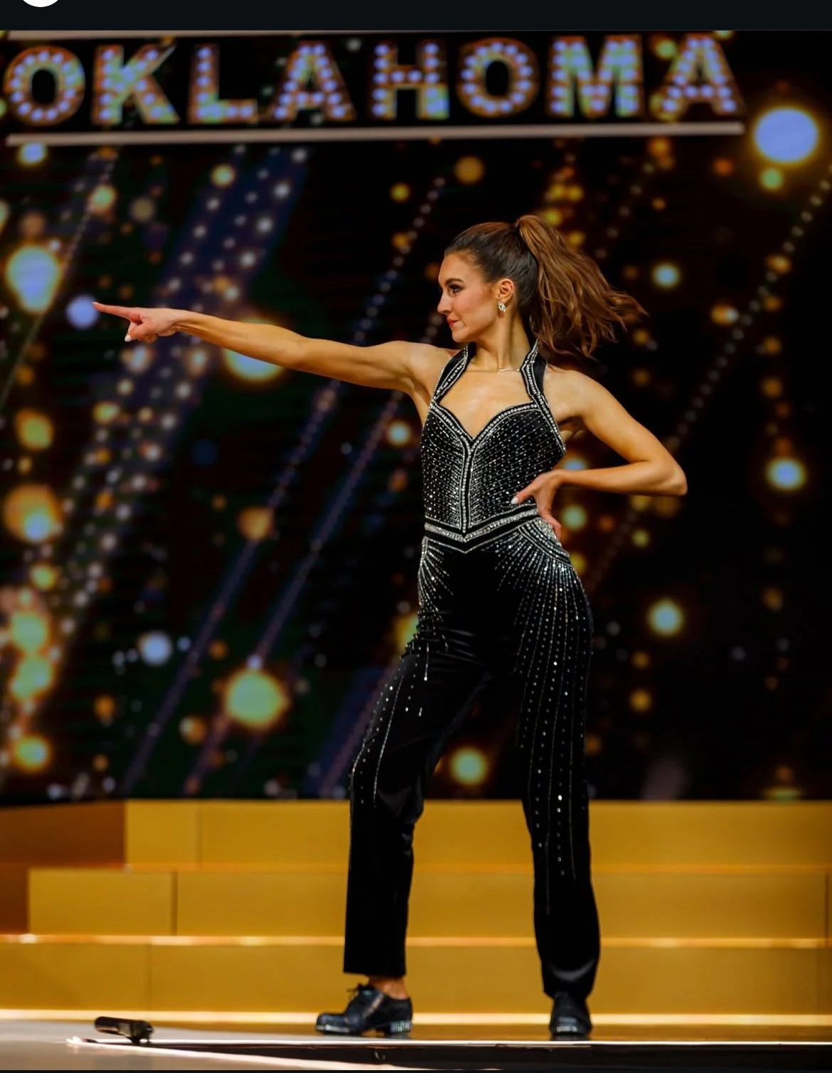 A woman performing a dance on stage during an Oklahoma-themed event, with a decorated background and gold steps.