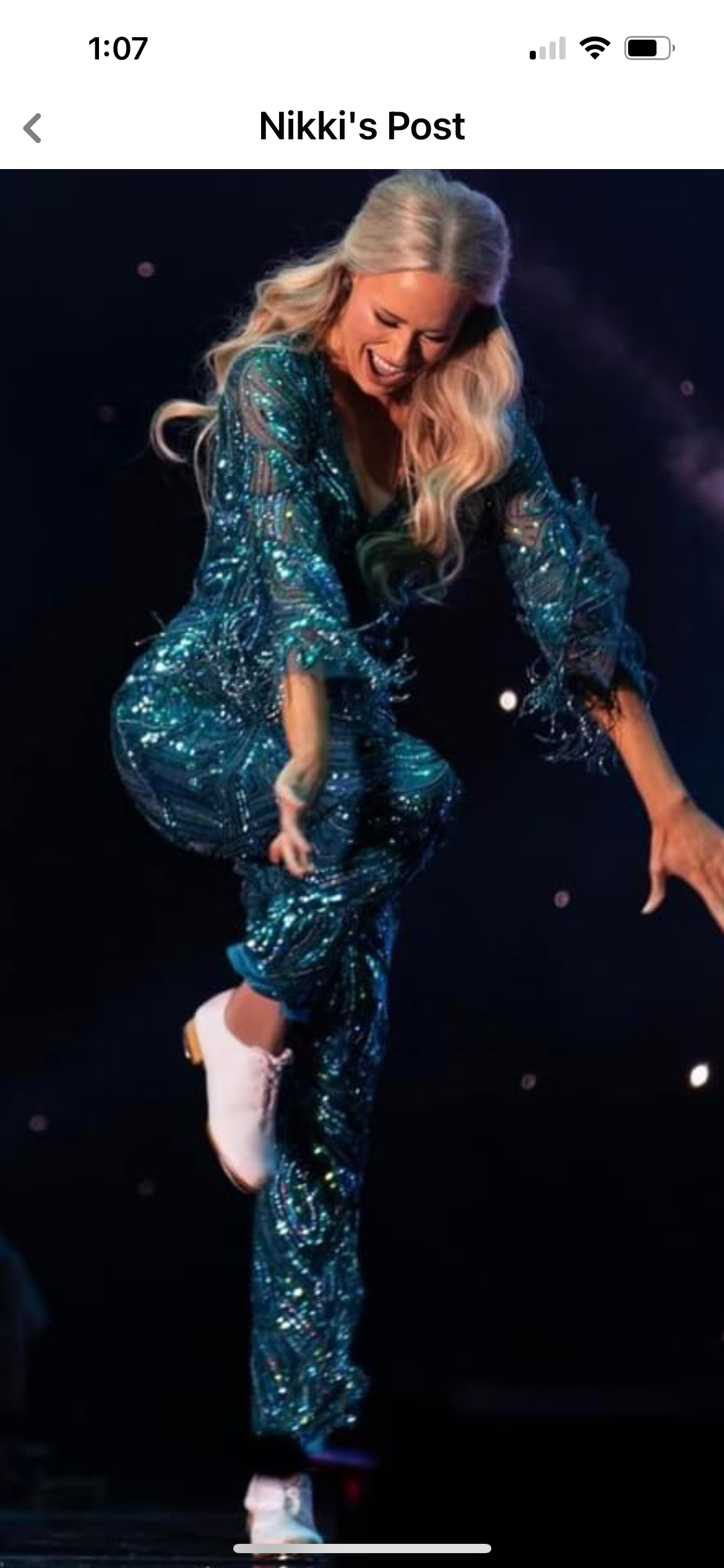 A woman with long blonde hair wearing a sparkly blue outfit and white ice skates, mid-performance on ice.