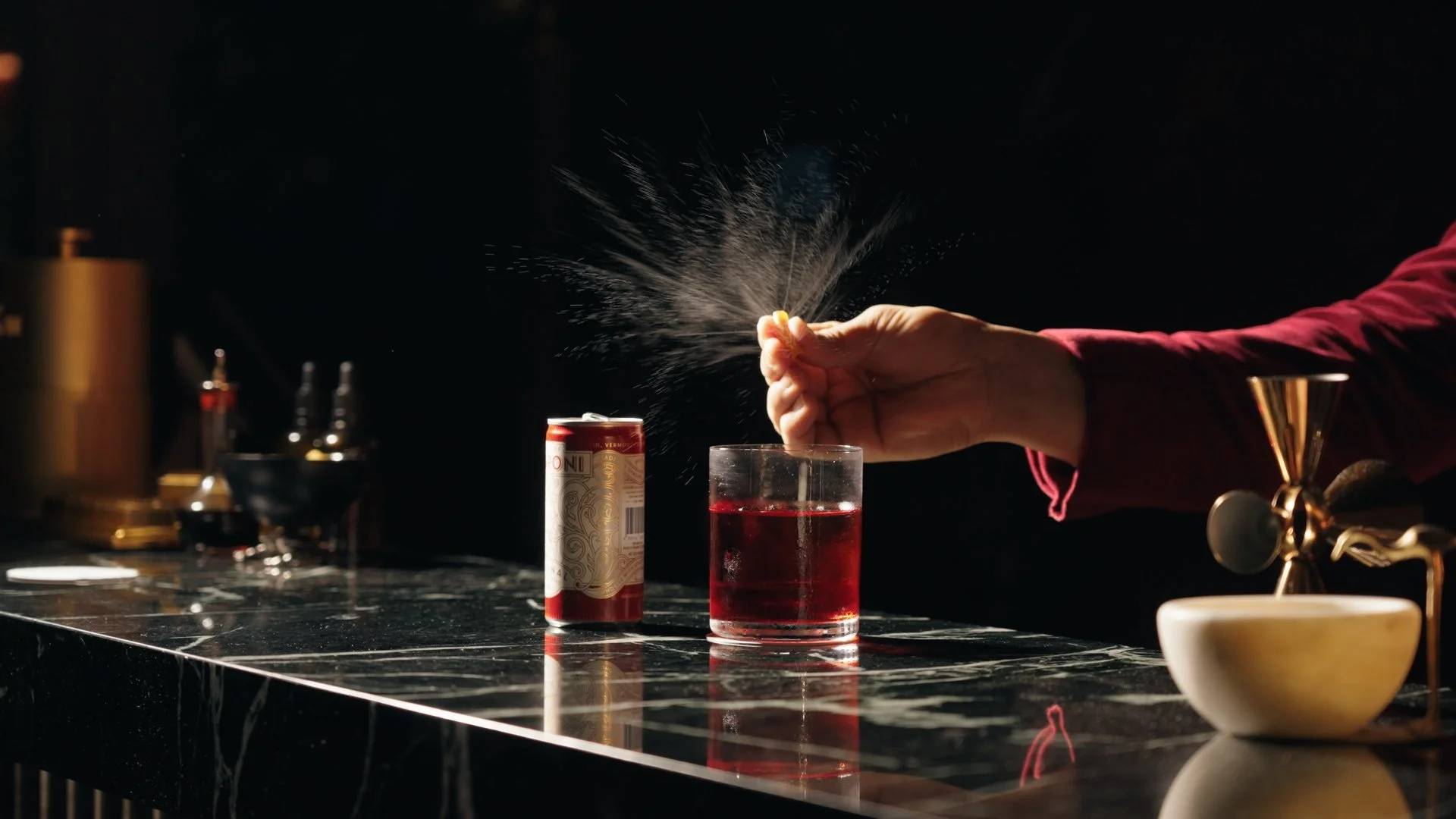 Person sprinkling a substance into a glass of red liquid on a dark bar counter, with bar tools and a can in the background.