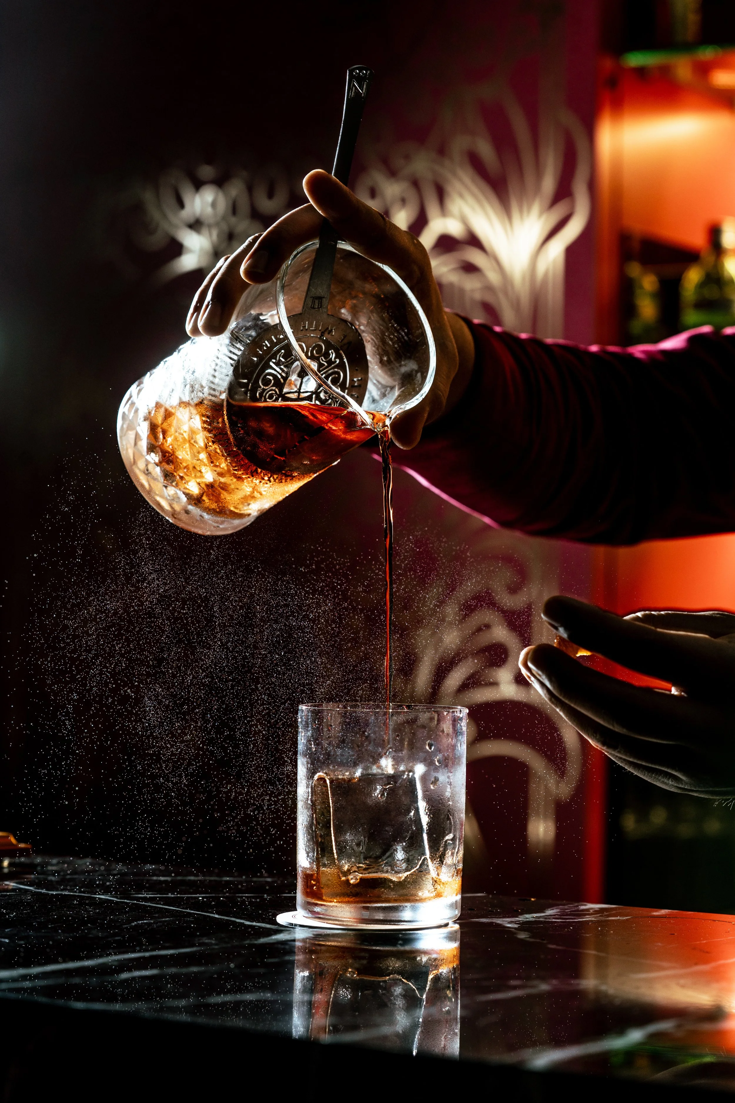 Bartender pouring negroni cocktail over ice in a bar