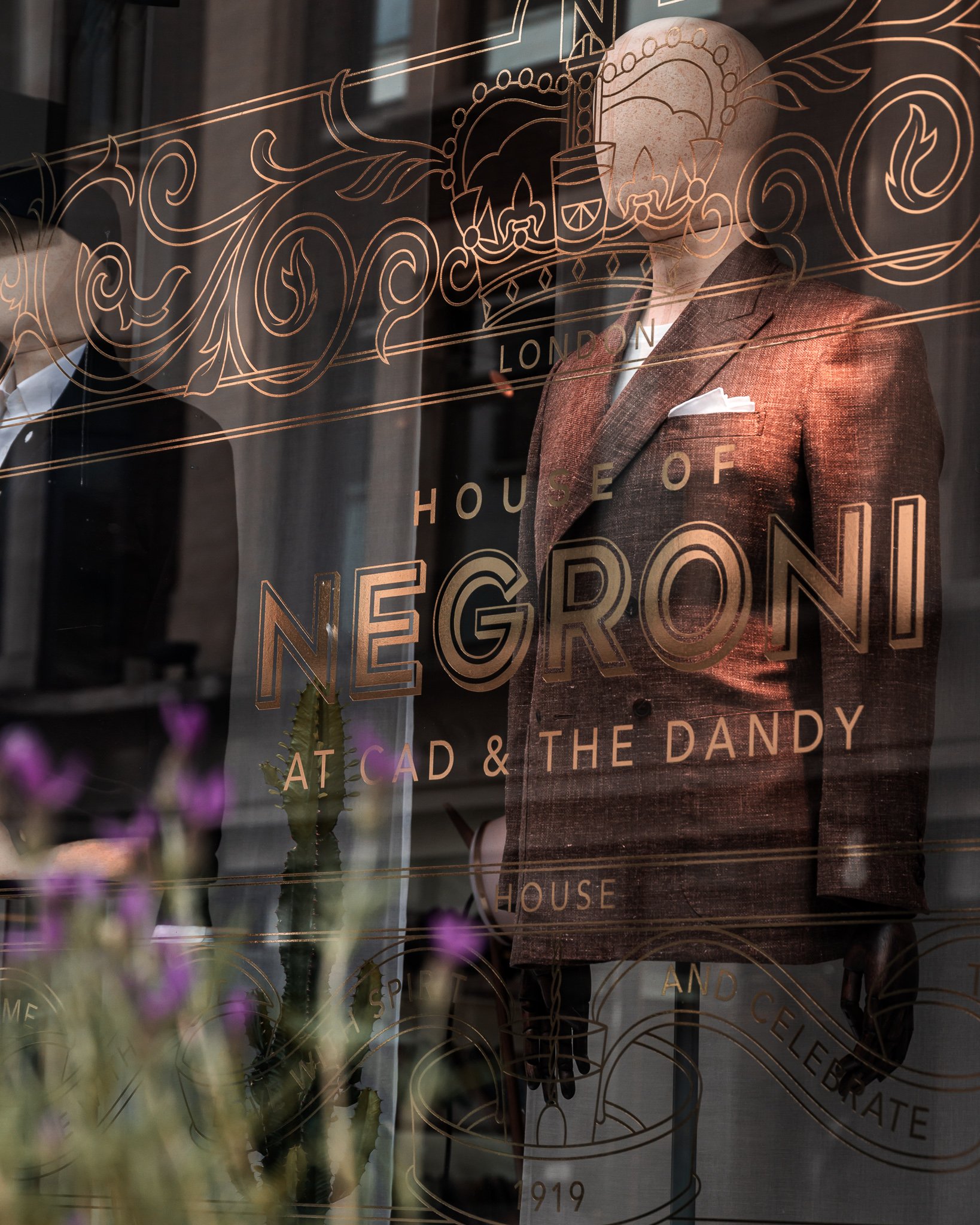 A Store front window with gold foling embellishments. It reads, House of Negroni at Cad and the Dandy, London House.
