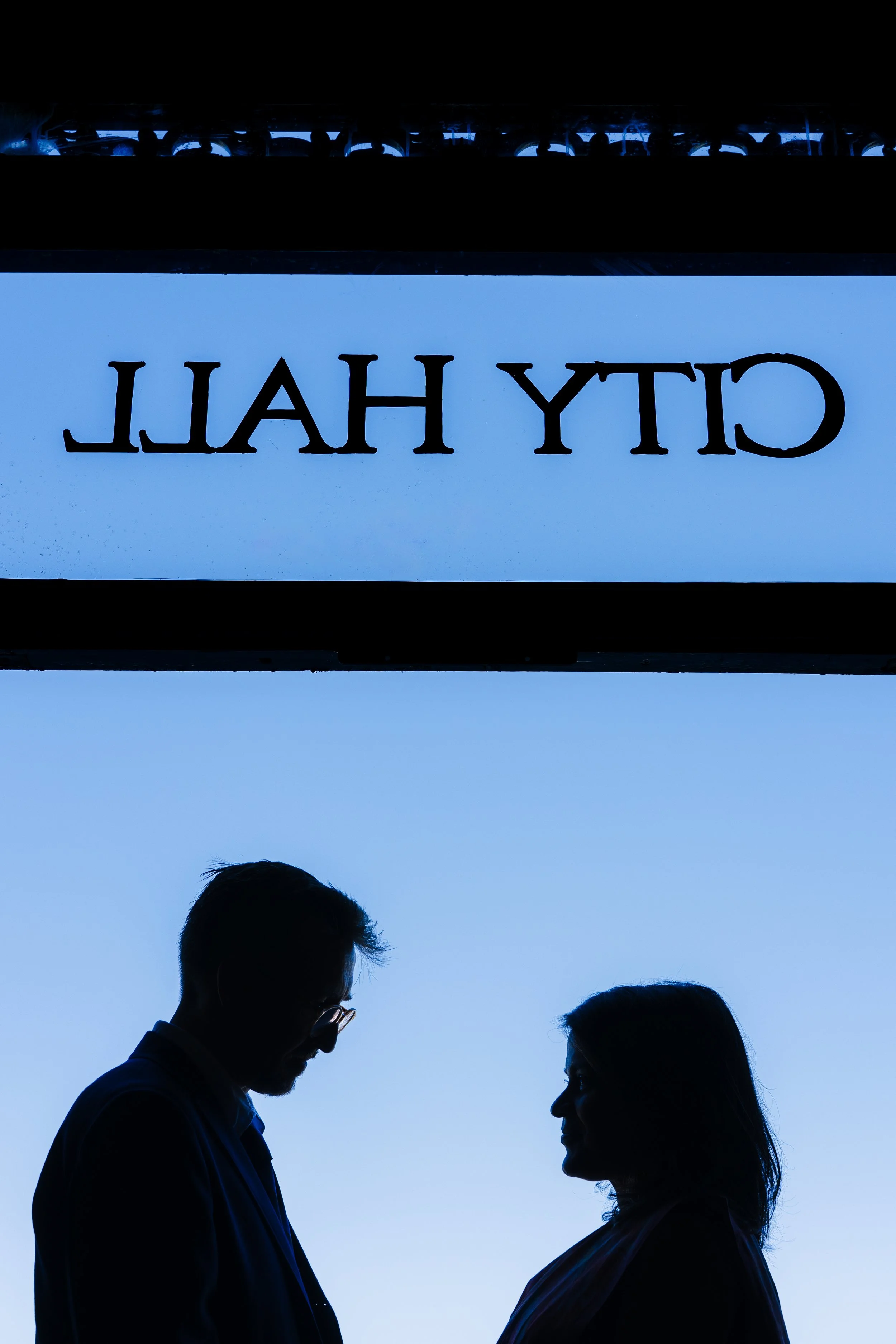 Silhouettes of a man and a woman facing each other against a clear blue sky, with a sign overhead reading 'CHICAGO' in reverse.