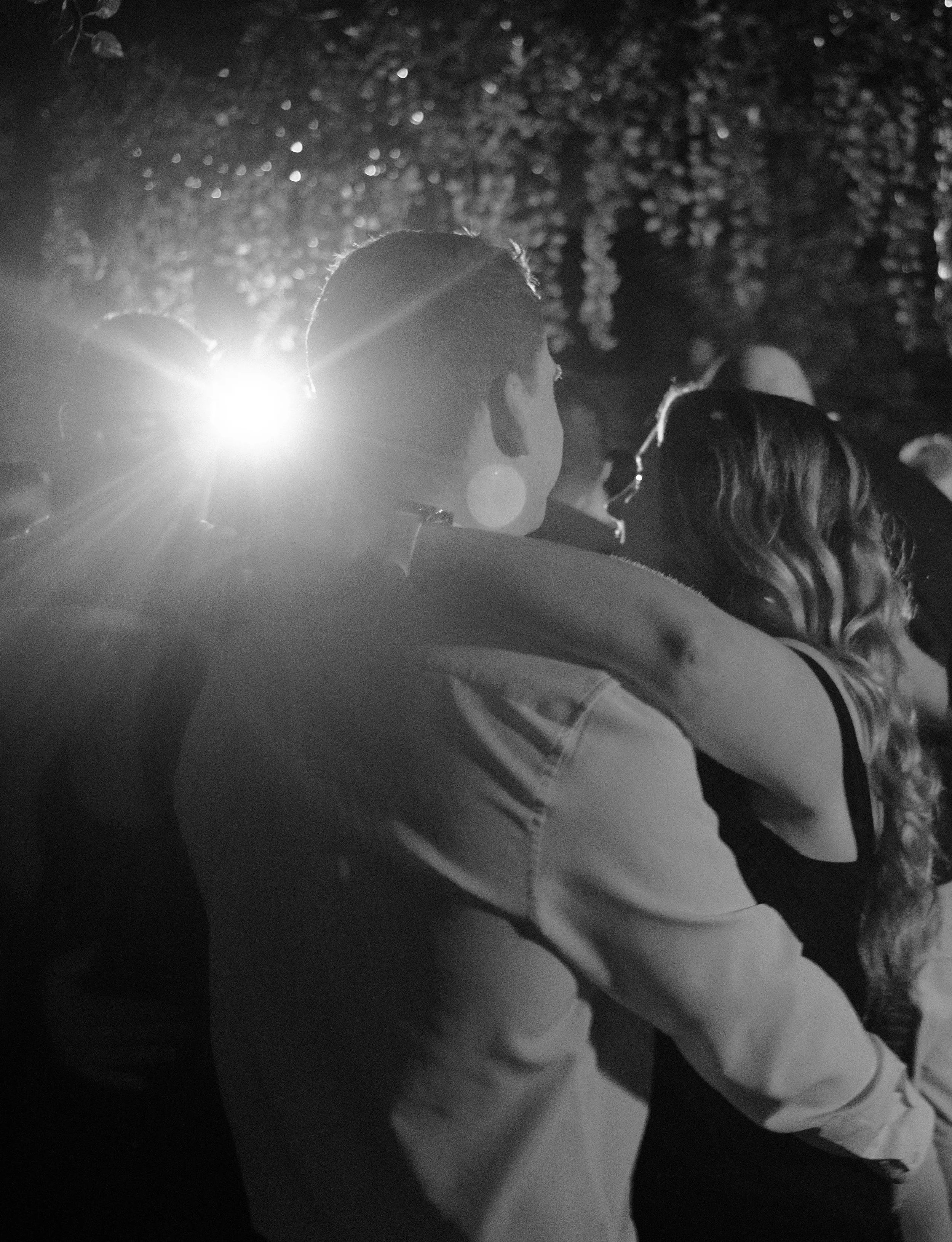 Couple embracing at night, with one person resting their head on the other's shoulder, in a black-and-white photograph. Planned by Shay from Shay does Weddings.