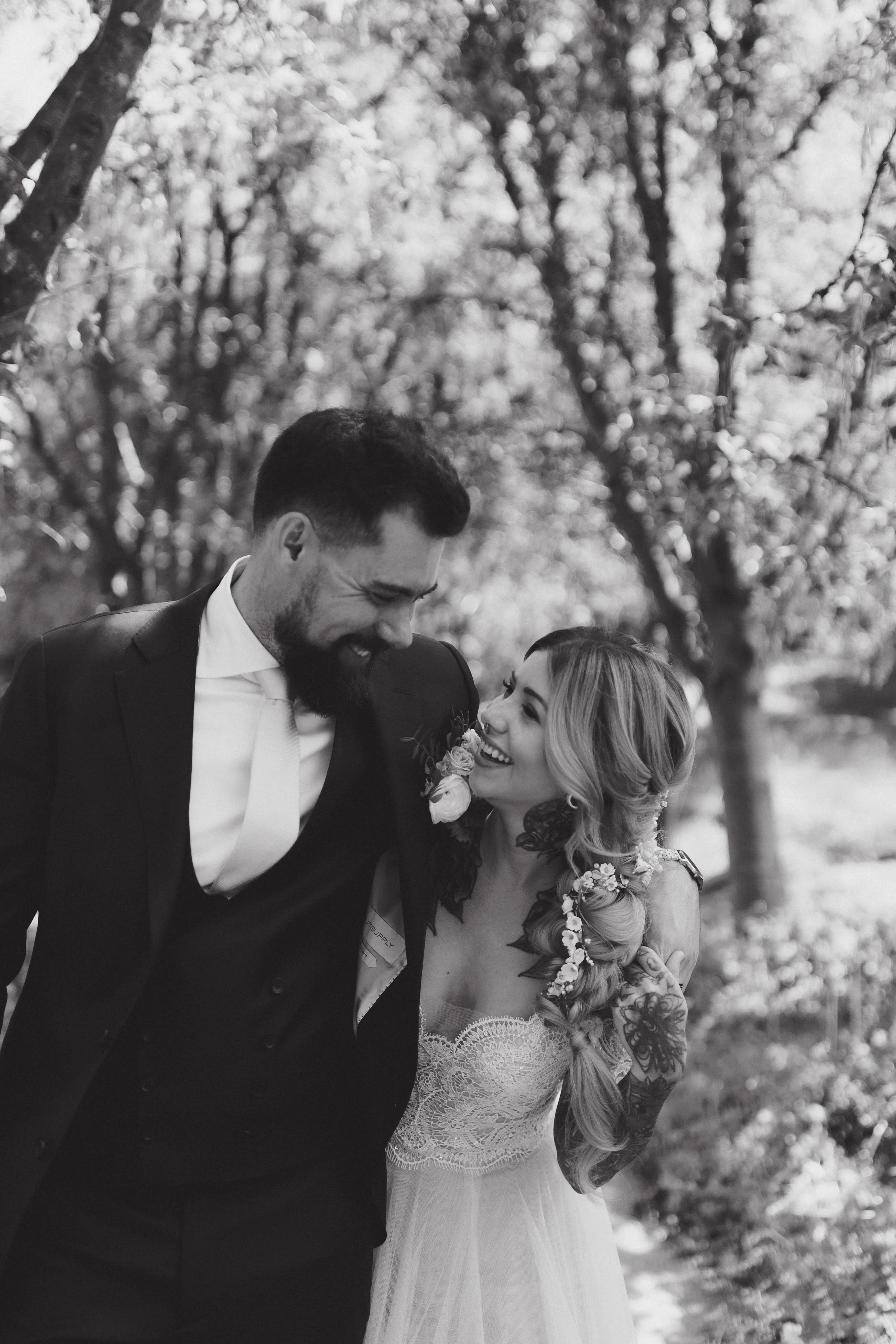 A smiling man in a suit and a woman in a wedding dress sharing a joyful moment outdoors among trees. Planned by Shay from Shay does Weddings.