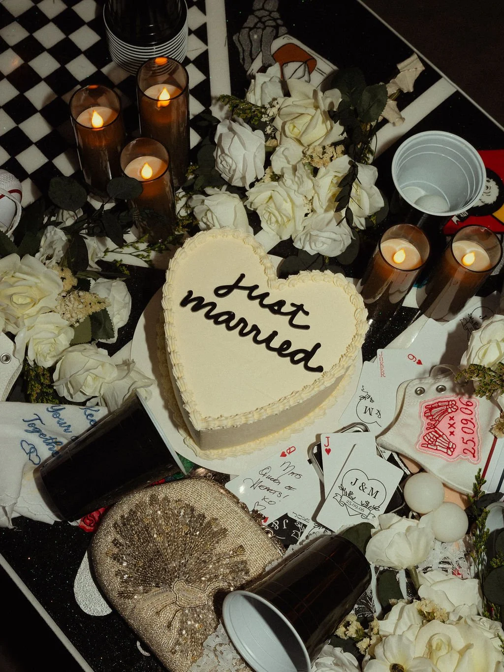 A wedding or engagement celebration display with a heart-shaped cake inscription 'just married,' surrounded by lit candles, white roses, playing cards, and decorative items. This is in Vancouver.