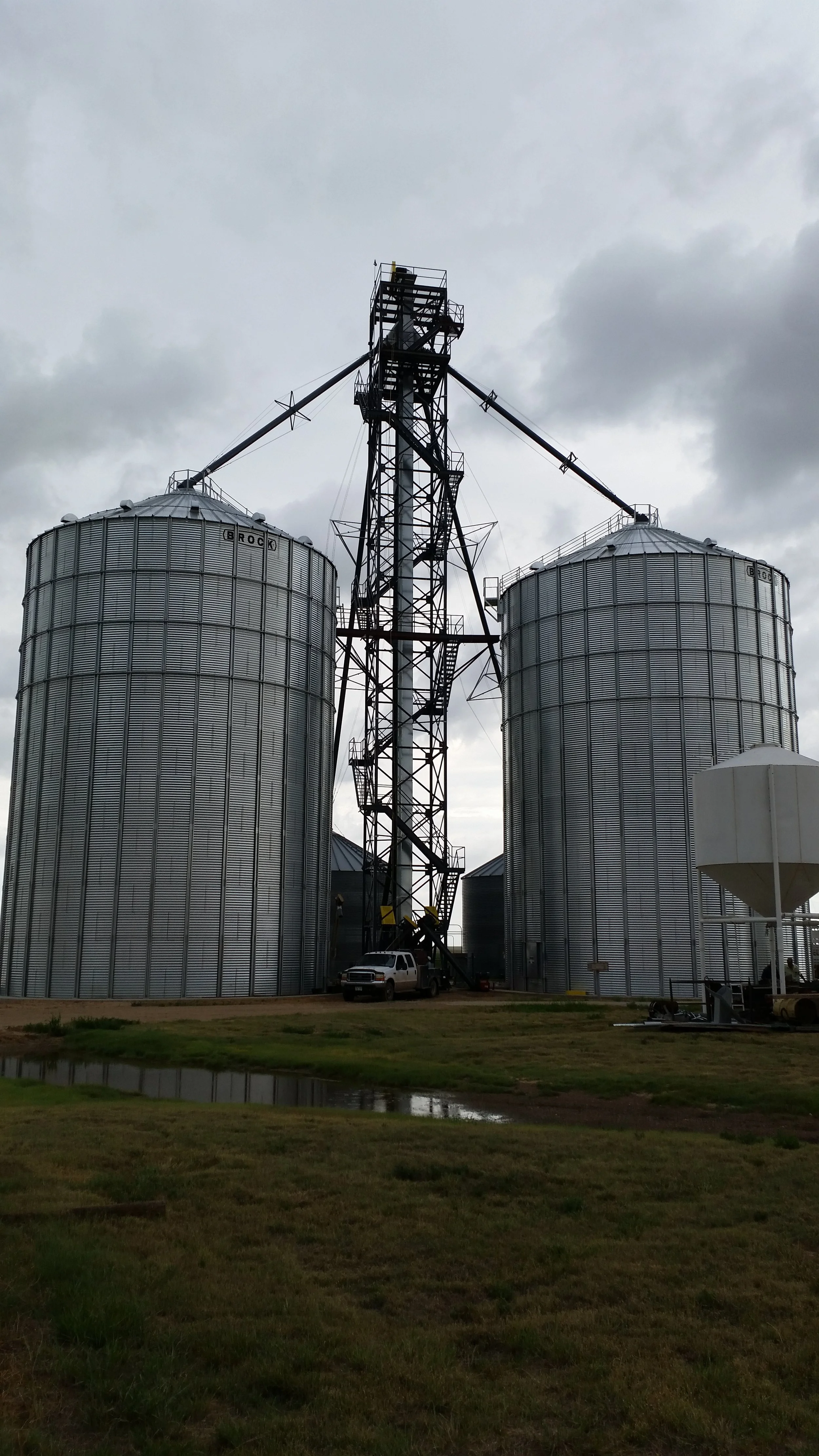 Two large metal grain silos with a tall black metal grain elevator structure connecting them.