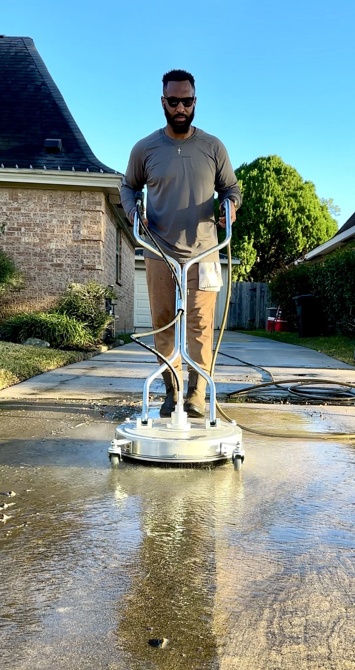Man cleaning a driveway with a power scrubber outside a house during daytime.