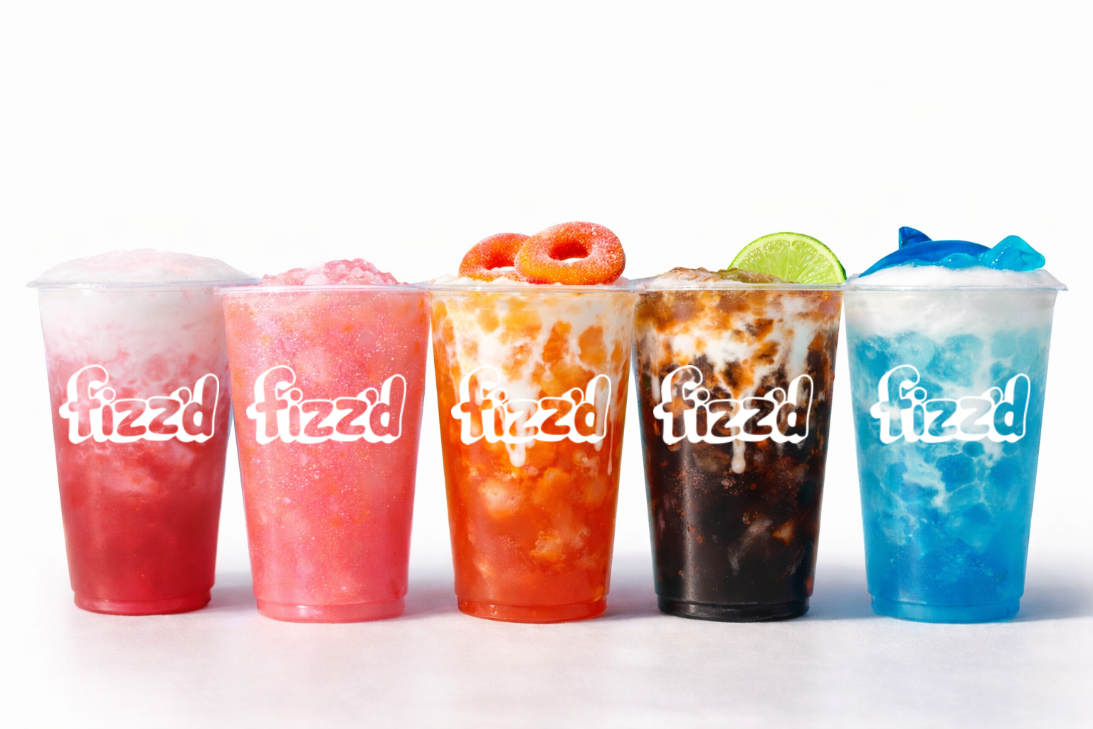 Five colorful frozen drinks in clear cups with the word "fizzd" on each, topped with ice and garnished with fruit slices and toppings.