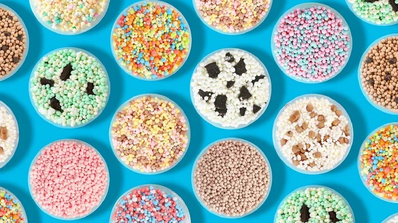 Assorted colorful sprinkles in small bowls on a blue background, many with animal faces like pandas and rabbits.