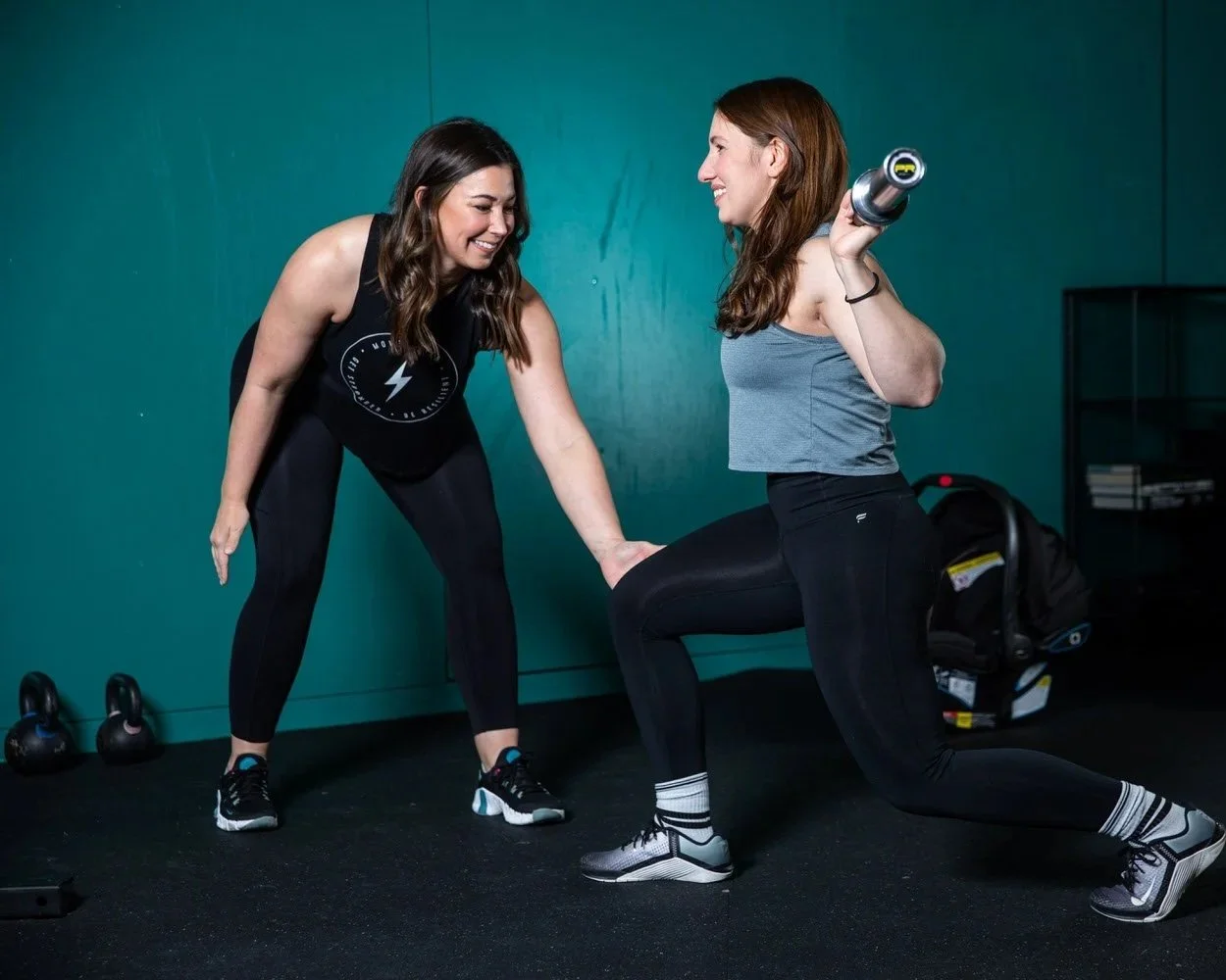 A physical therapist giving a tactile cue to a patient's knee to decrease knee valgus during a barbell back rack lunge.