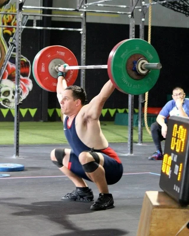 Coach Rick Meldrum performing a squat snatch while training in an Olympic weightlifting facility.