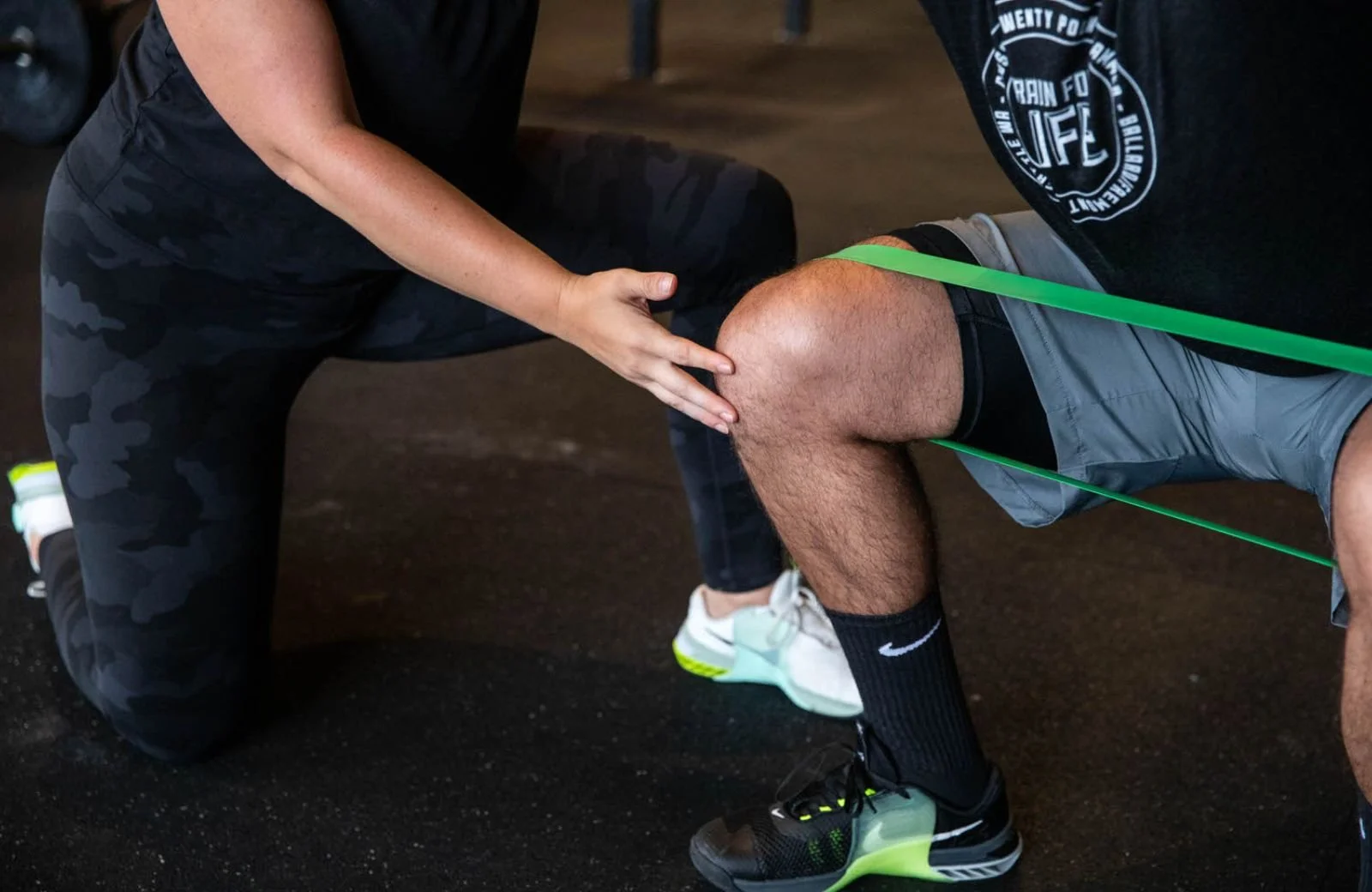 A physical therapist assists a patient with knee pain with resistance band exercises during a workout at the gym.