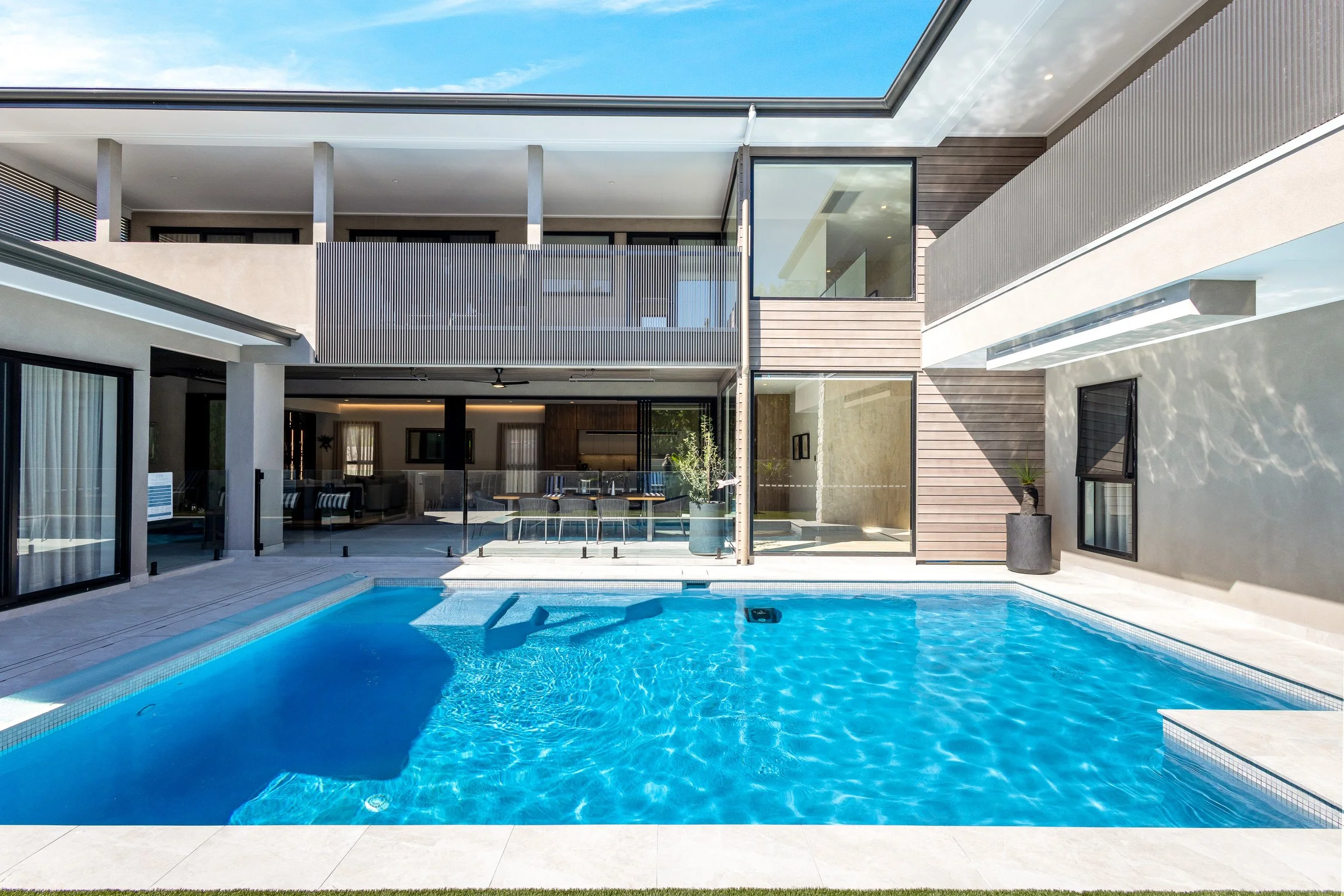Modern house with a backyard swimming pool, glass doors, and balconies, under a clear blue sky.
