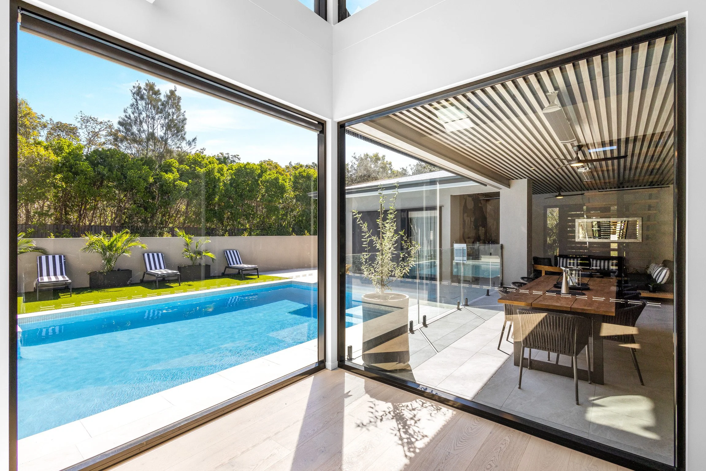Modern living room with large glass sliding doors opening to a backyard with swimming pool, lounge chairs, and greenery.