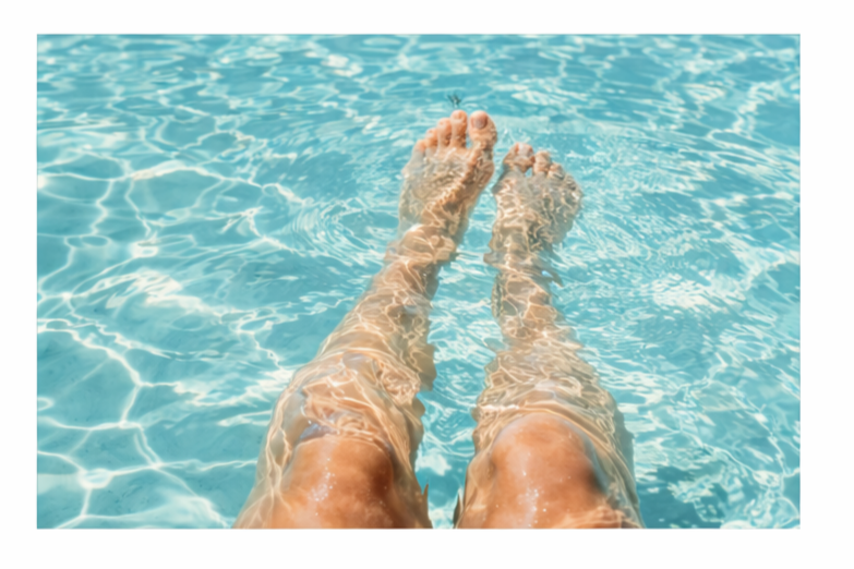 A person relaxing in a swimming pool with legs and feet submerged in the water.