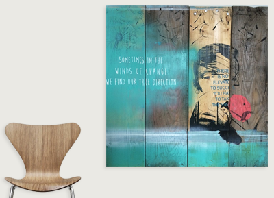 Colorful street art mural on a wooden wall panel with quote and abstract imagery, next to a wooden chair.