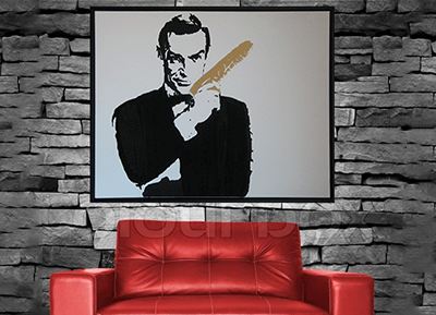 Plaque with a stencil portrait of a man holding a comb, hanging on a stone wall above a red leather sofa.