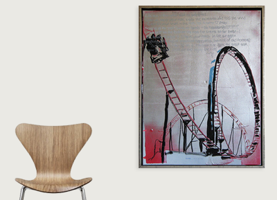 A framed art print of a roller coaster with a steep drop, hanging on a plain white wall next to a wooden chair with a curved backrest.