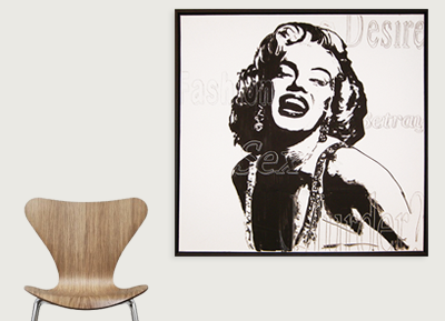 A black and white portrait of Marilyn Monroe on a wall, with a wooden chair below it.