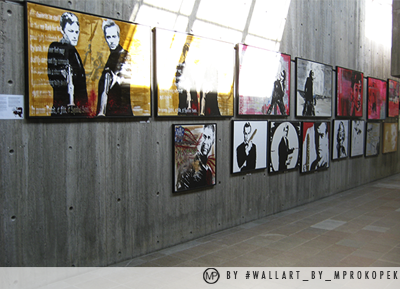 A series of posters on a concrete wall, including images of two men, some abstract designs, and various artistic black-and-white and colored images.