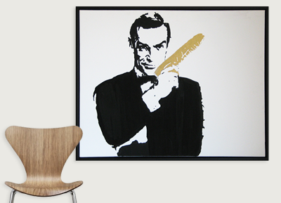 A framed black and white artwork of a man holding a golden feather, with a wooden chair nearby.