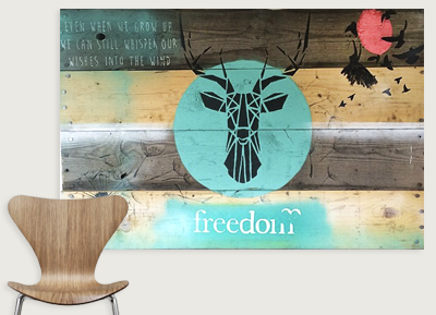 Wall art with a giraffe's head silhouette inside a blue circle, the word "freedom" below, a red bird, and handwritten text on wooden planks.