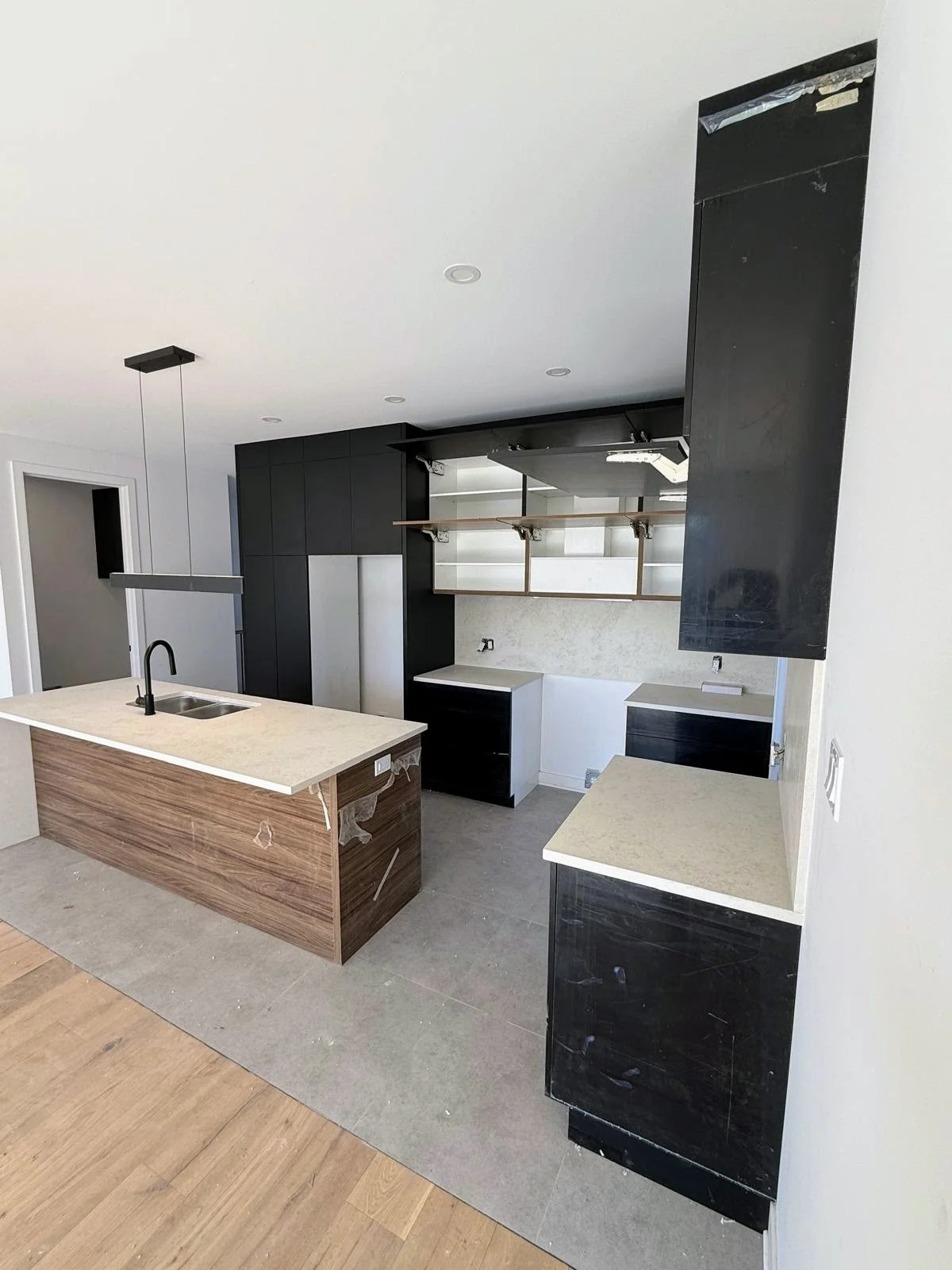Kitchen under construction with a central island, black cabinets, open shelves, and unconnected appliances.